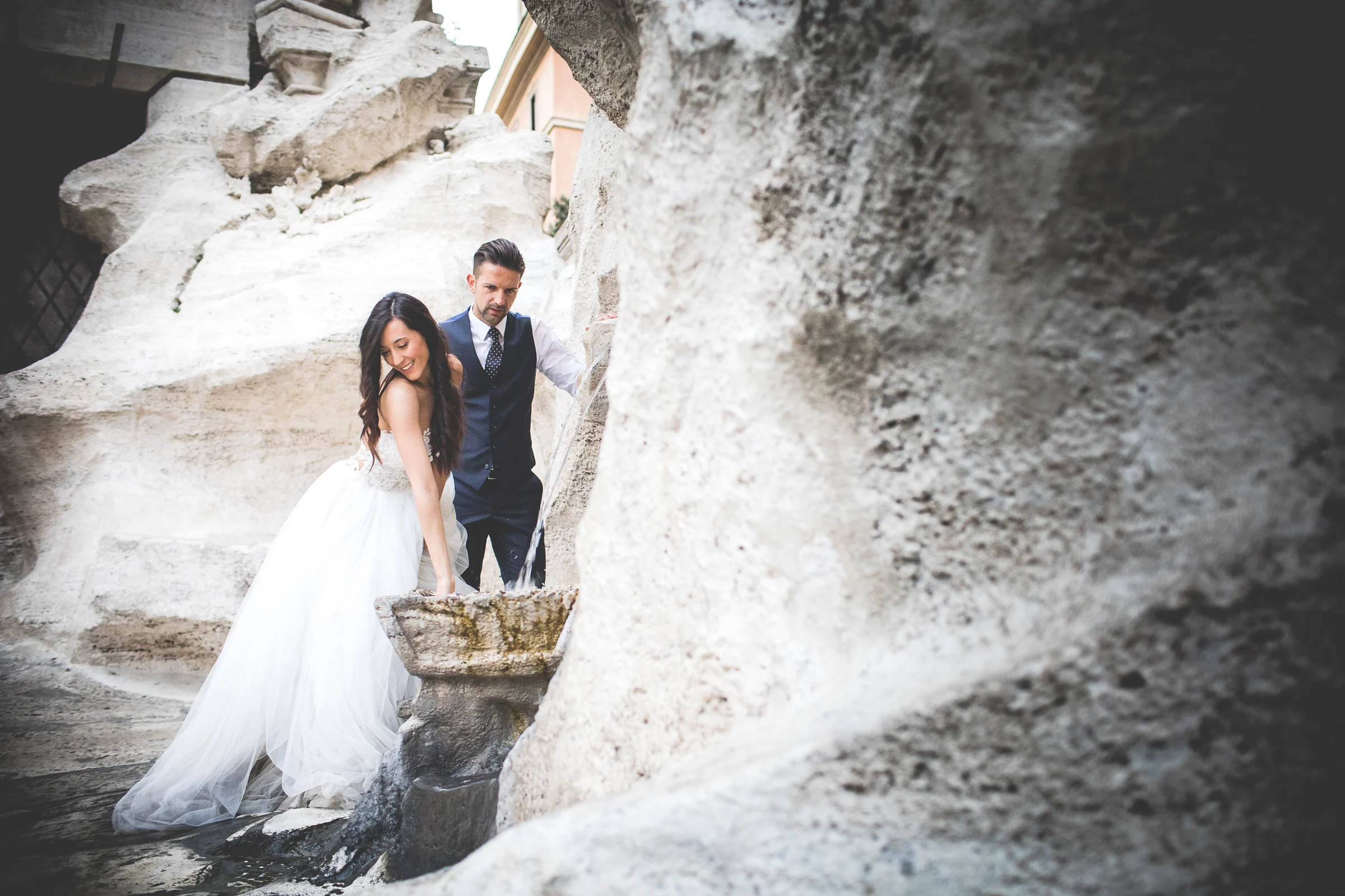 Los novios exploran un rincón de roca de la Fontana di Trevi durante una sesión postboda en Fontana di Trevi.