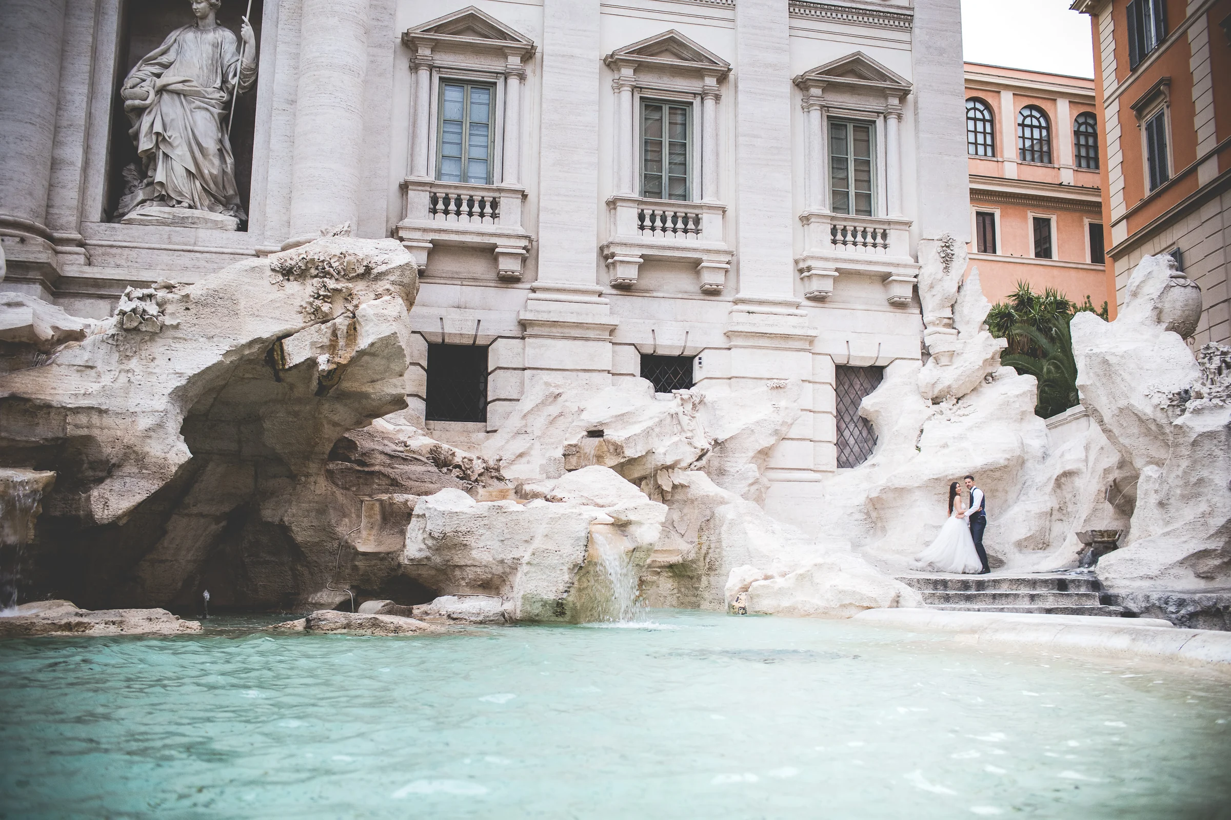 Vista amplia lateral de la Fontana di Trevi con la pareja al fondo durante una sesión postboda en Fontana di Trevi.