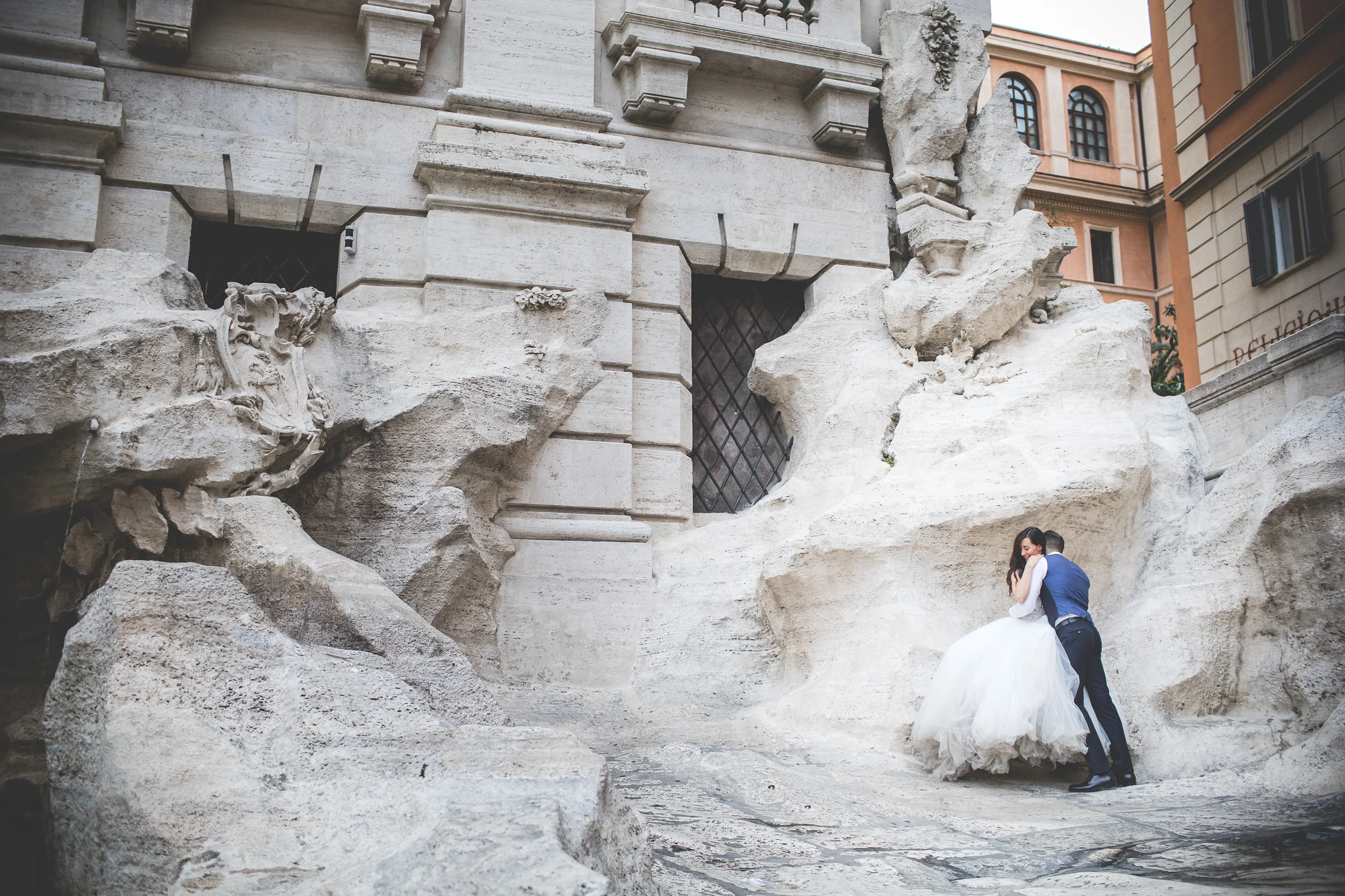 Los novios abrazados entre las rocas escultóricas de la Fontana di Trevi durante una sesión postboda en Fontana di Trevi.