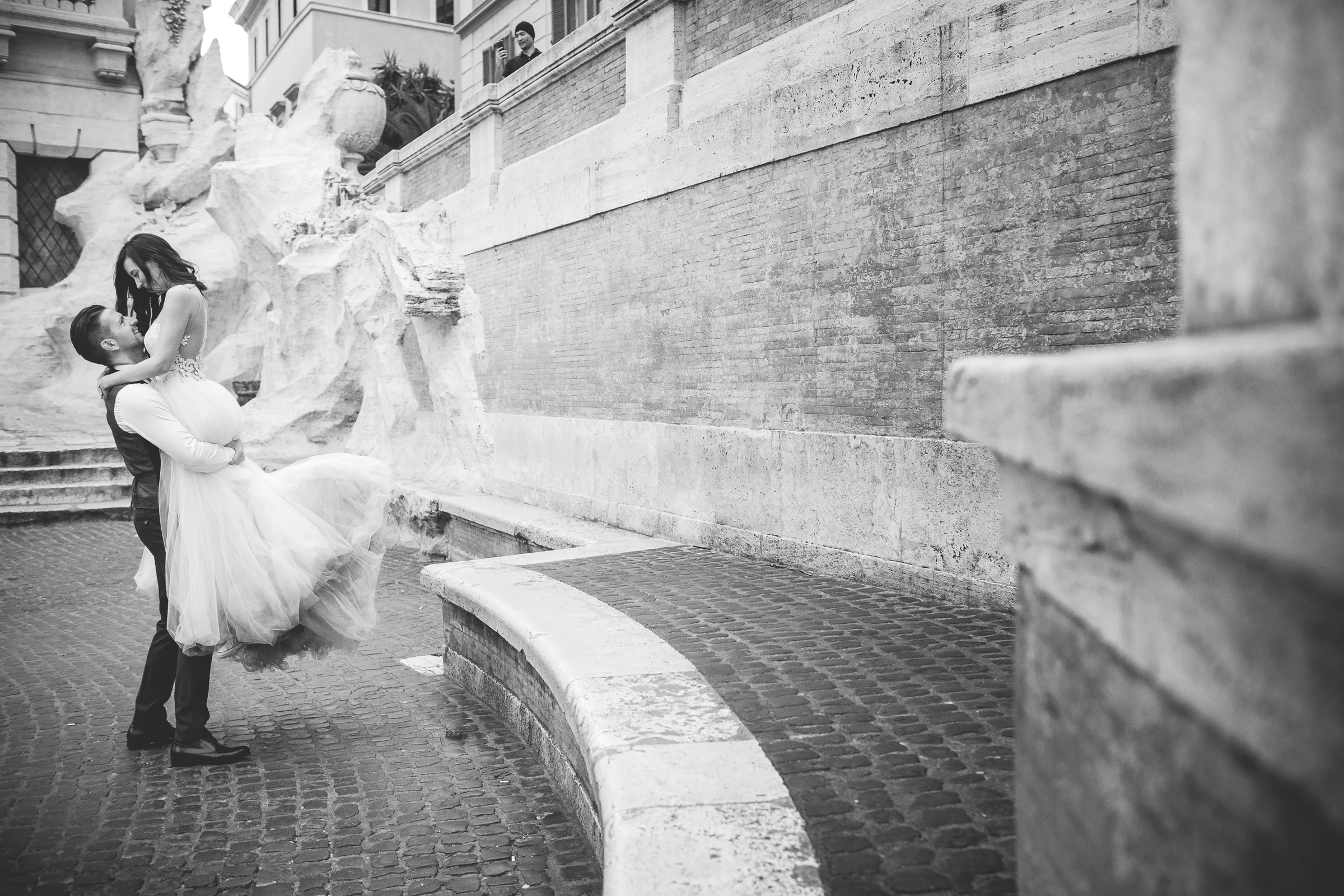 Retrato en blanco y negro del novio levantando a la novia junto a la Fontana di Trevi durante una sesión postboda en Fontana di Trevi.