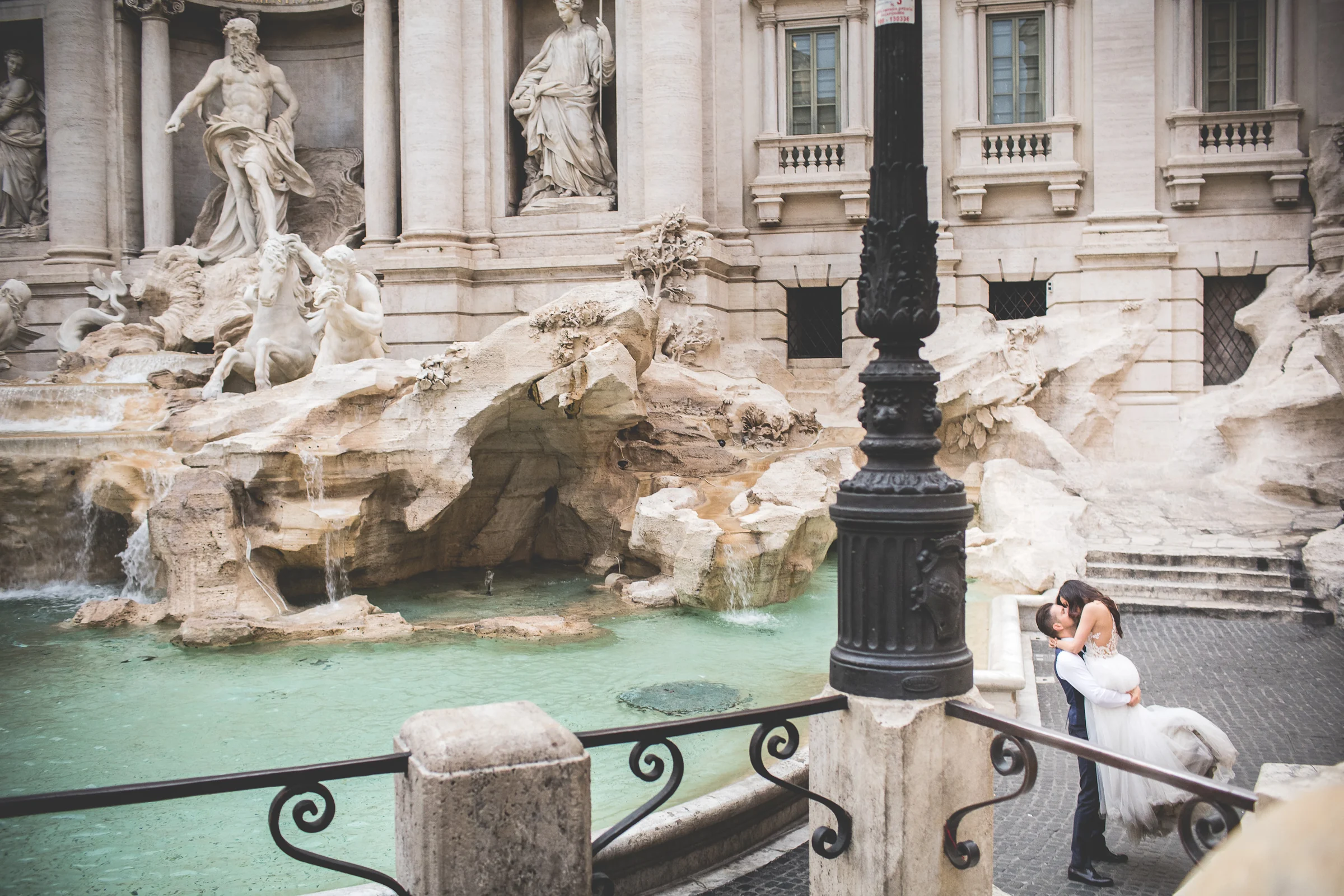 Vista elevada de la Fontana di Trevi con la pareja abrazada en una esquina durante una sesión postboda en Fontana di Trevi.