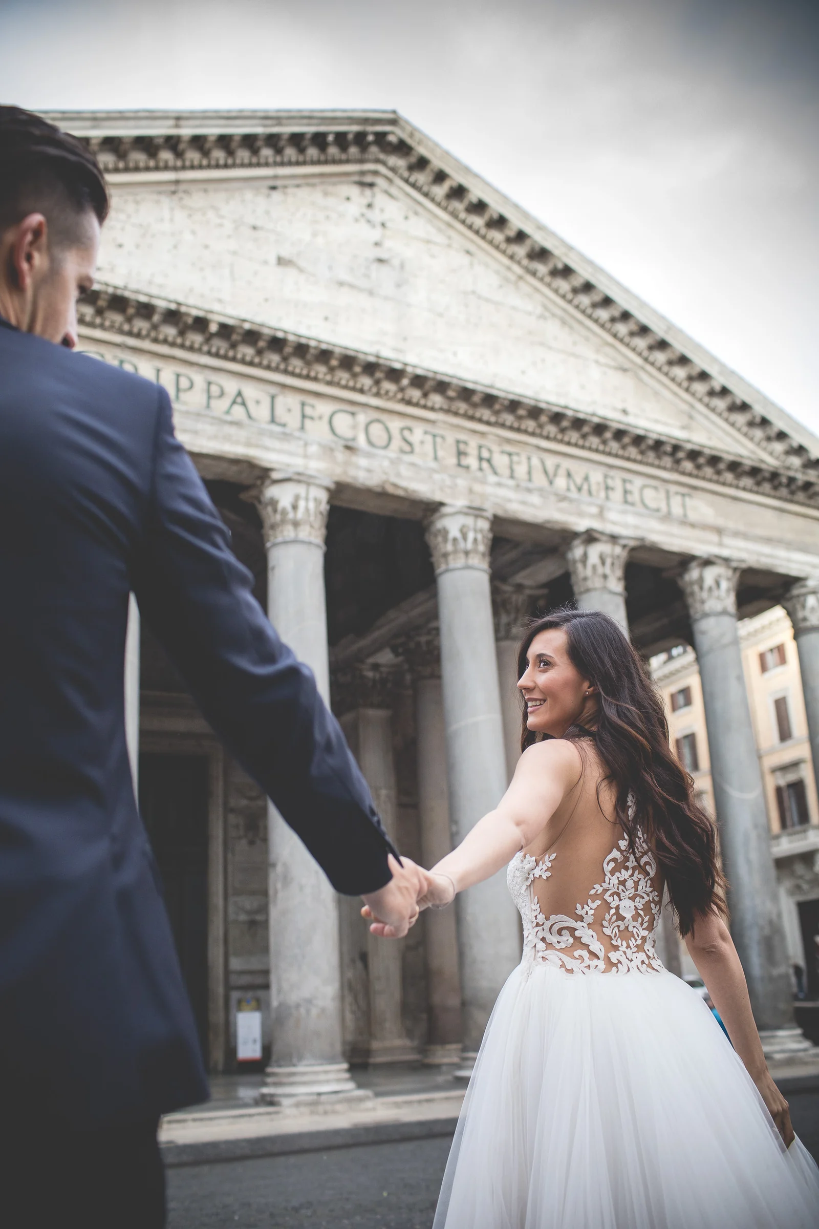 La novia mira al novio mientras caminan de la mano frente al Panteón durante una sesión postboda en Panteón de Roma.