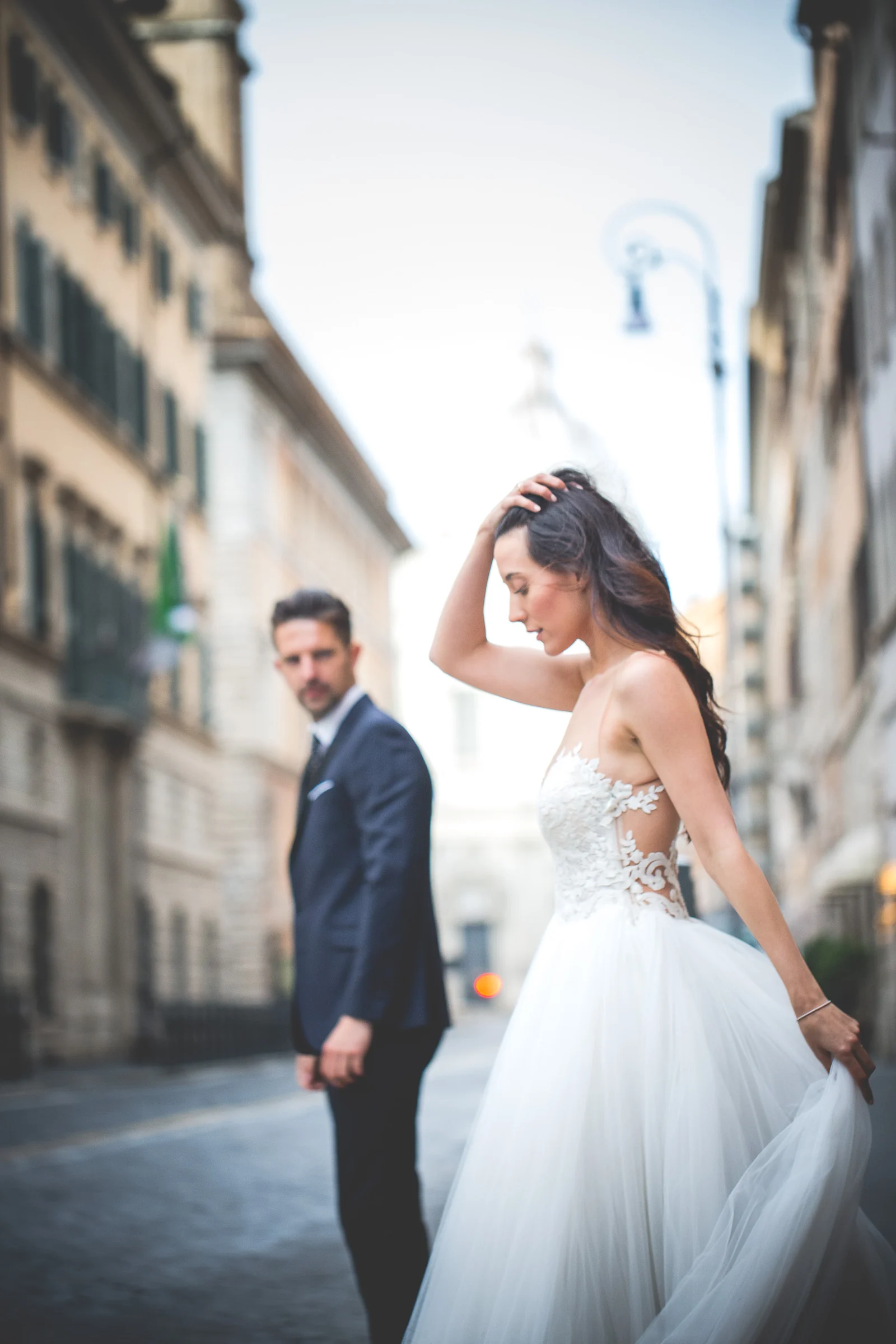 Retrato de la novia en movimiento con el novio desenfocado en una calle romana durante una sesión postboda en Panteón de Roma.