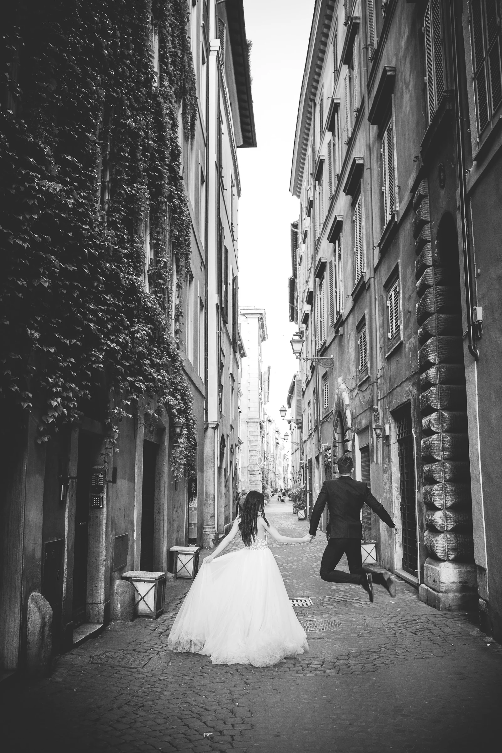 La pareja recorre de espaldas una calle estrecha del centro histórico en blanco y negro durante una sesión postboda en Centro histórico de Roma.