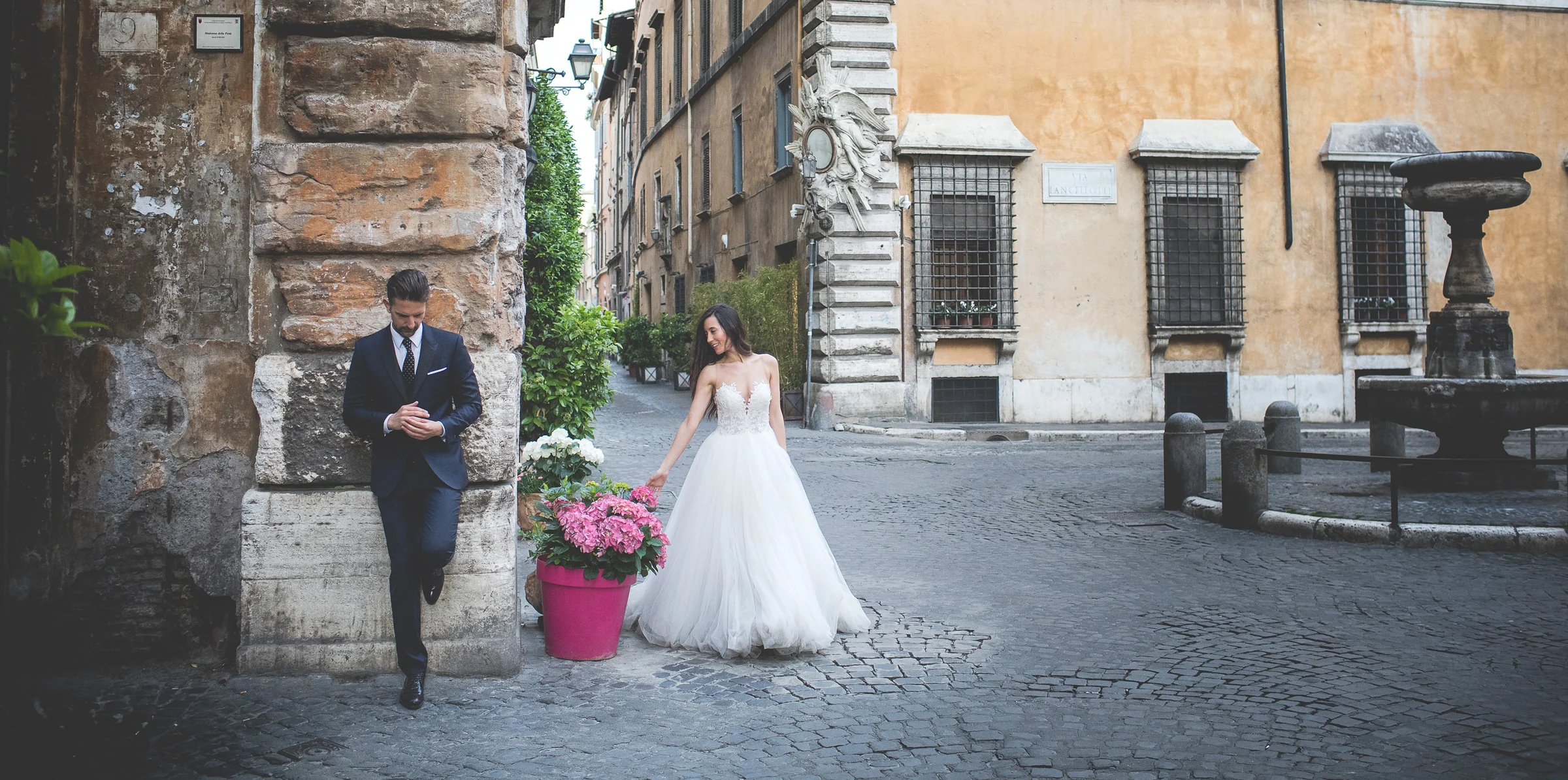 Los novios se separan jugando en una pequeña plaza adoquinada con flores durante una sesión postboda en Centro histórico de Roma.