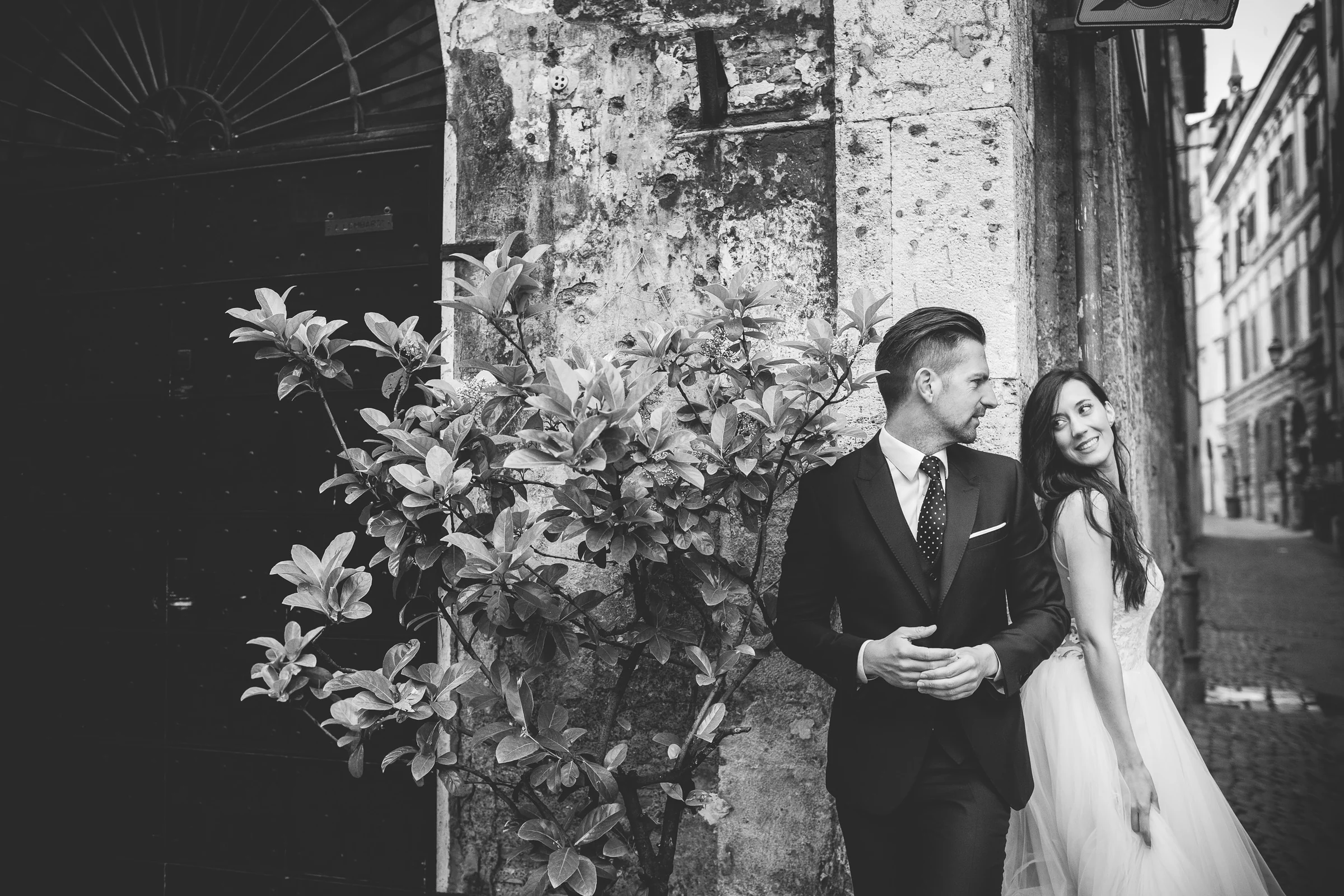 Retrato en blanco y negro de la pareja junto a un muro antiguo y vegetación durante una sesión postboda en Centro histórico de Roma.