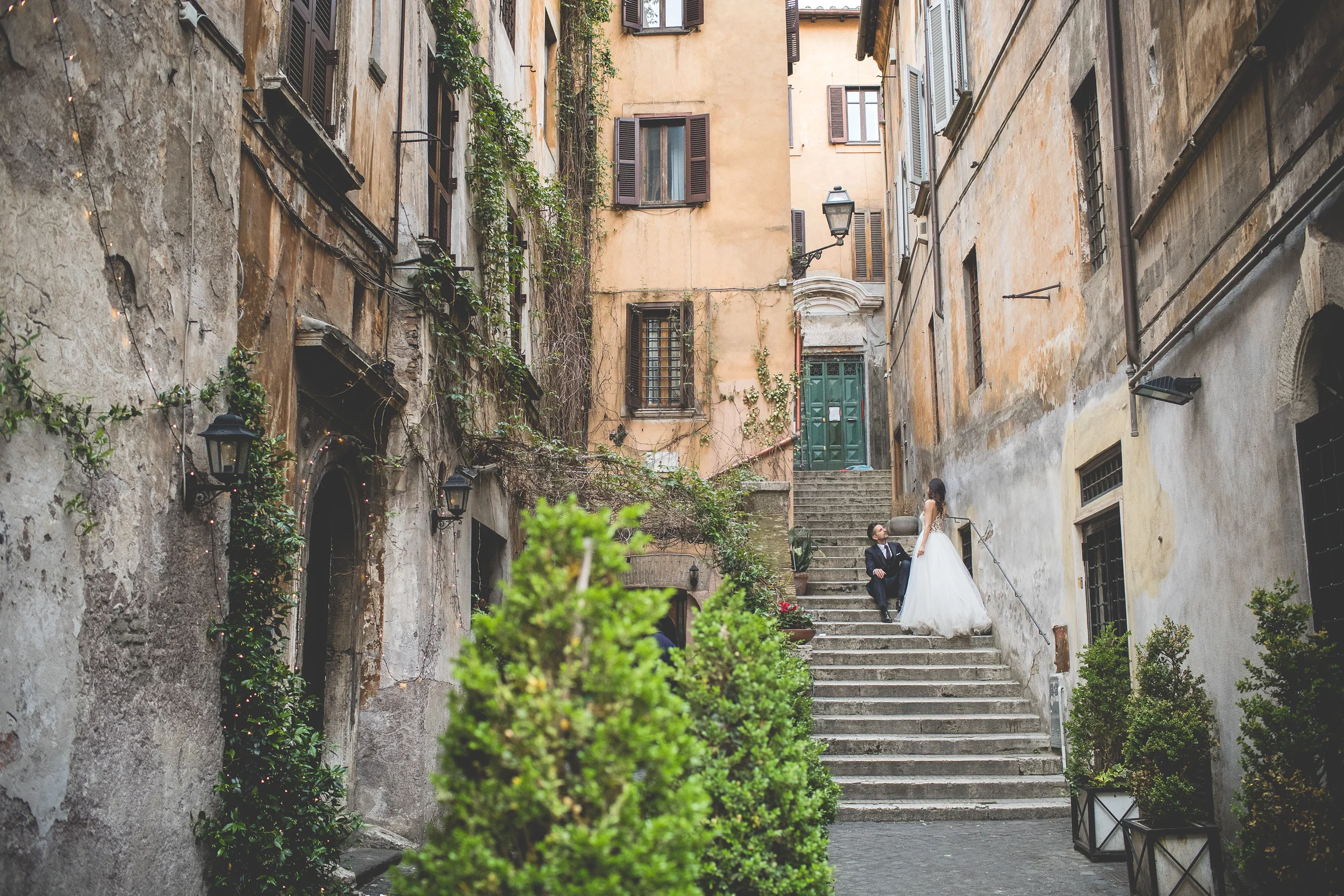 Vista amplia de una escalinata y calle antigua con los novios al fondo durante una sesión postboda en Centro histórico de Roma.