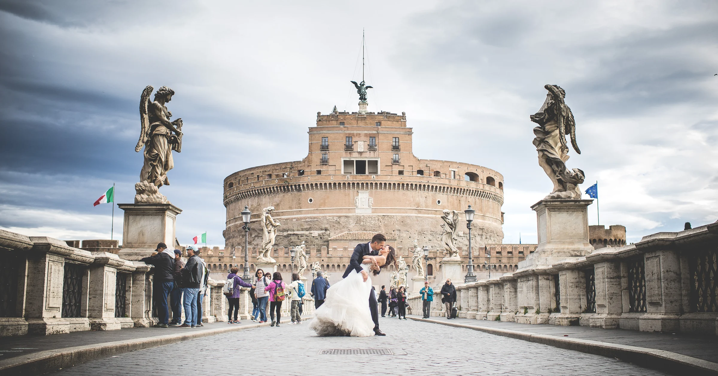 La pareja posa en el Ponte Sant’Angelo con Castel Sant’Angelo al fondo durante una sesión postboda en Ponte Sant’Angelo y río Tíber.