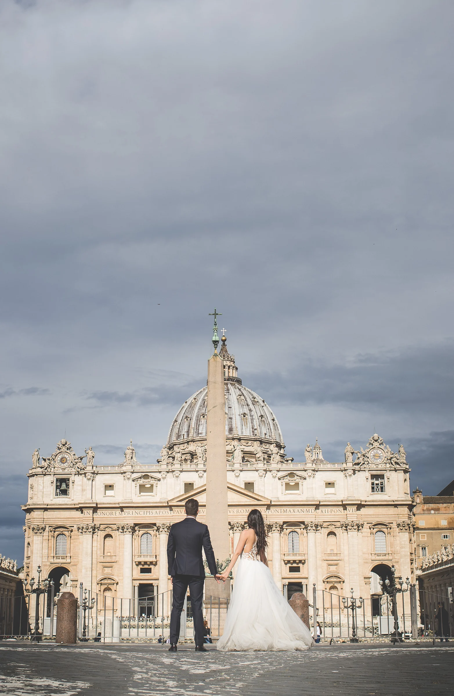 La pareja de espaldas contempla la Basílica de San Pedro y el obelisco de la plaza durante una sesión postboda en Vaticano y Plaza de San Pedro.