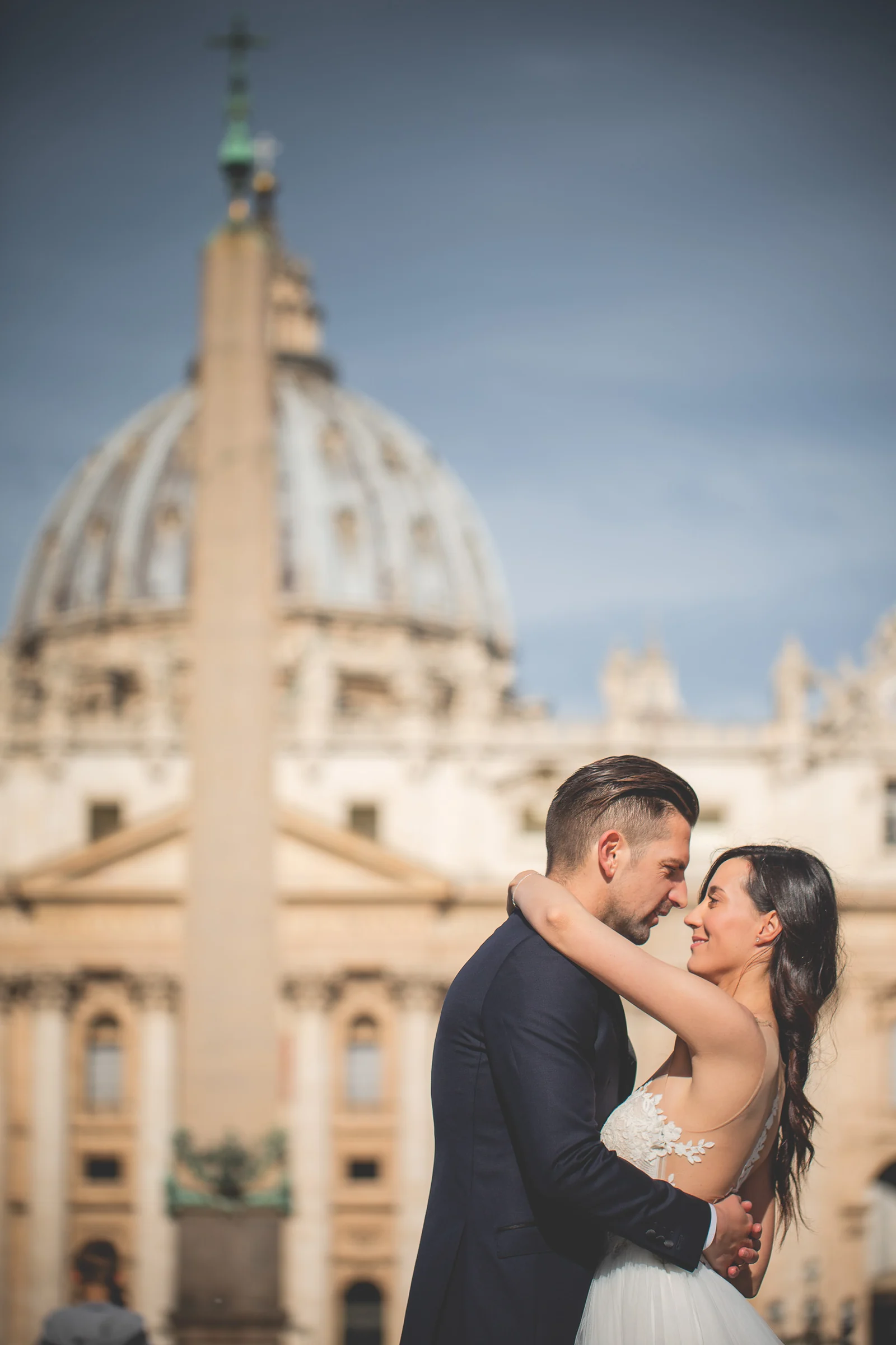 Primer plano de los novios abrazados con la cúpula de San Pedro desenfocada al fondo durante una sesión postboda en Vaticano y Plaza de San Pedro.