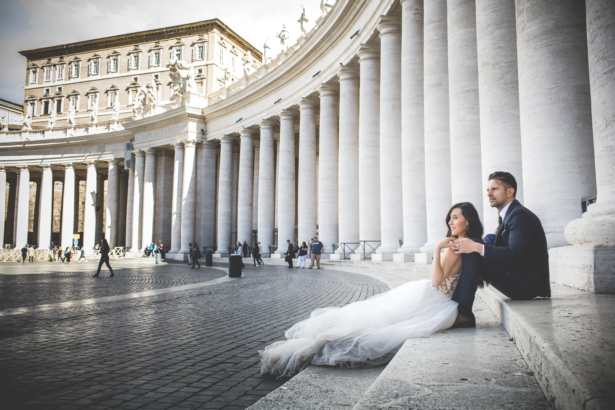 Los novios sentados junto a la columnata de la Plaza de San Pedro durante una sesión postboda en Vaticano y Plaza de San Pedro.