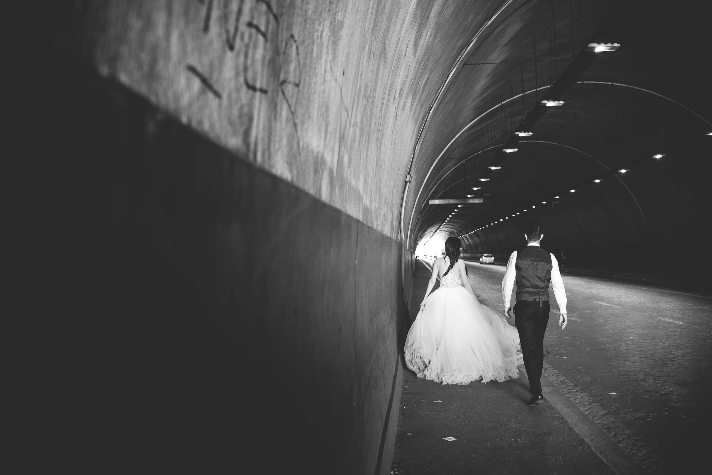 Los novios caminan de espaldas por un túnel romano en blanco y negro durante una sesión postboda en Túnel urbano de Roma.