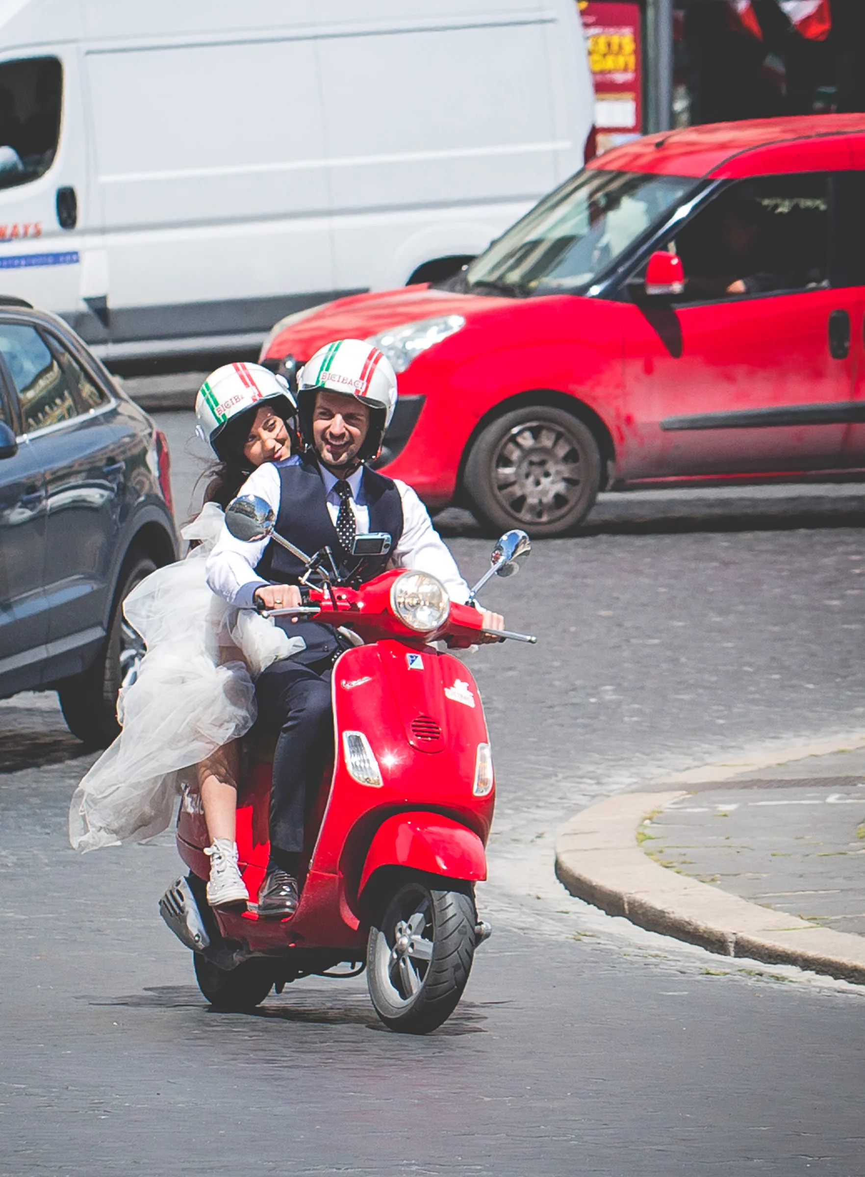 La pareja circula en una Vespa roja por las calles de Roma con el vestido al viento durante una sesión postboda en Calles de Roma con Vespa.