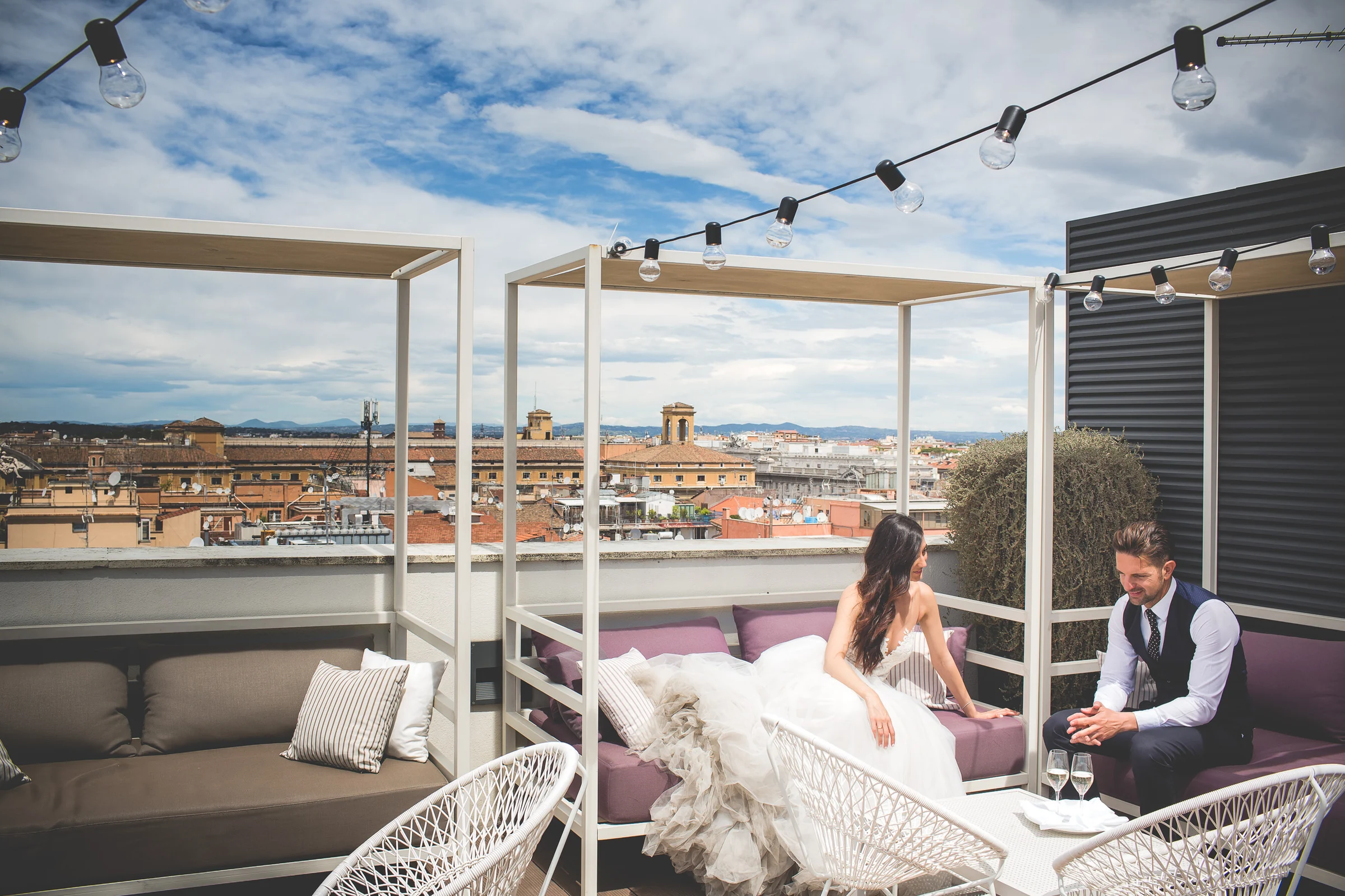 Los novios conversan sentados en una terraza panorámica de Roma durante una sesión postboda en Terraza panorámica de Roma.