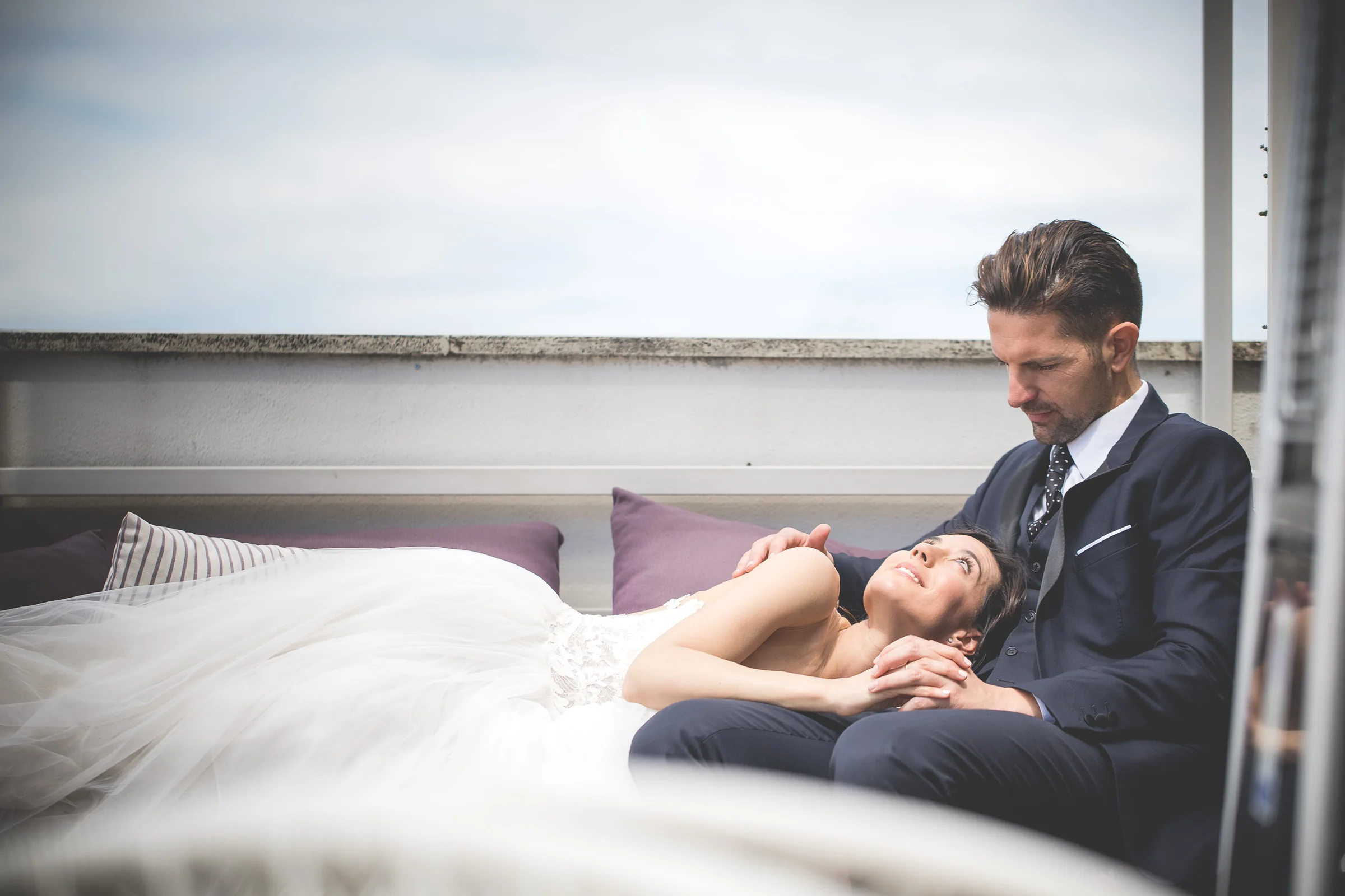 La novia descansa recostada sobre el novio en una terraza panorámica al final de la sesión durante una sesión postboda en Terraza panorámica de Roma.
