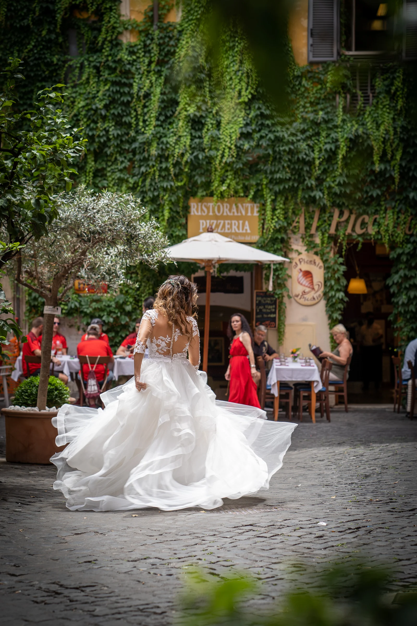 Esther caminando con su vestido de novia por una calle adoquinada del centro histórico de Roma entre terrazas y vegetación.