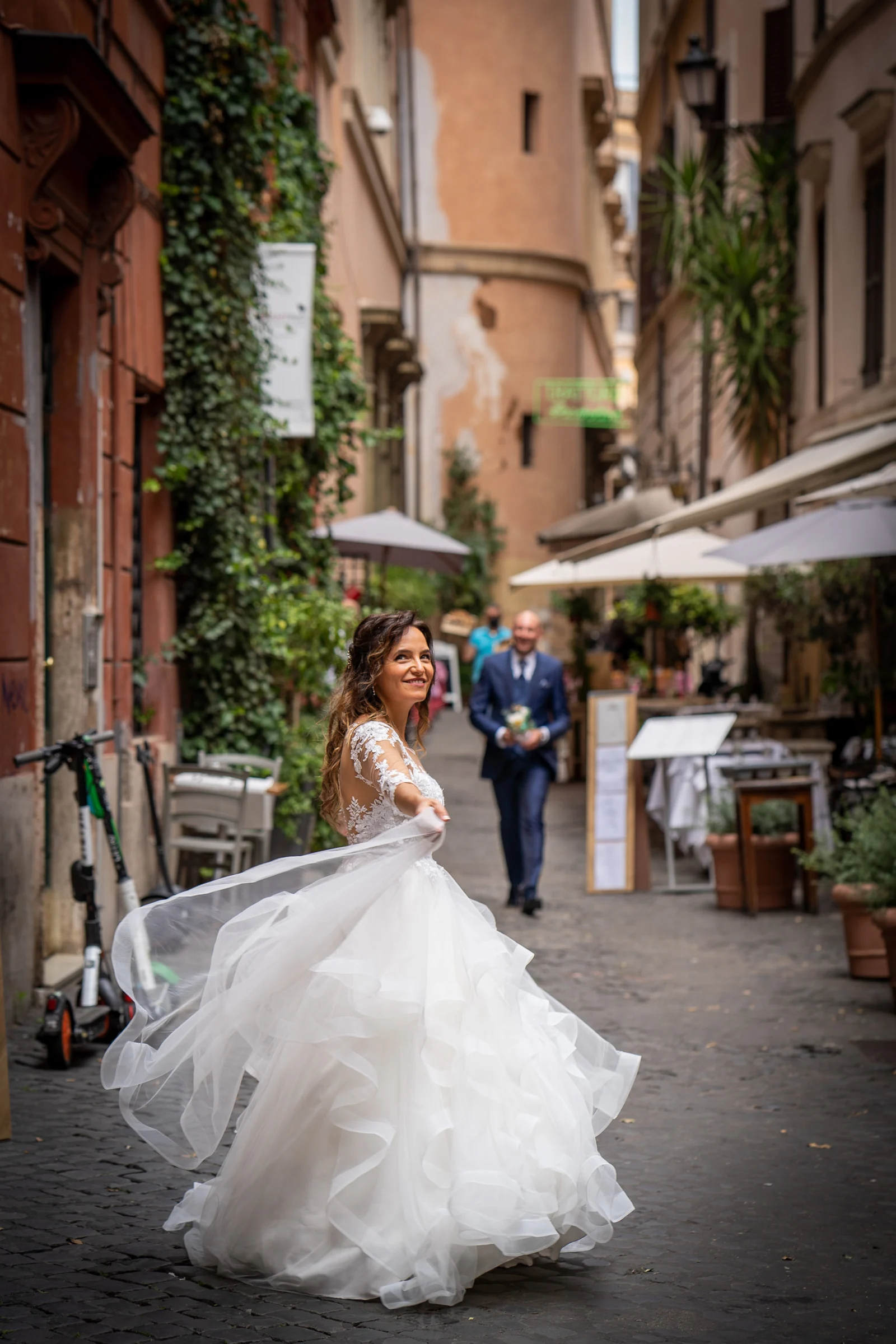Esther gira sonriente con el vestido en movimiento mientras Marco aparece al fondo de una calle del centro histórico de Roma.
