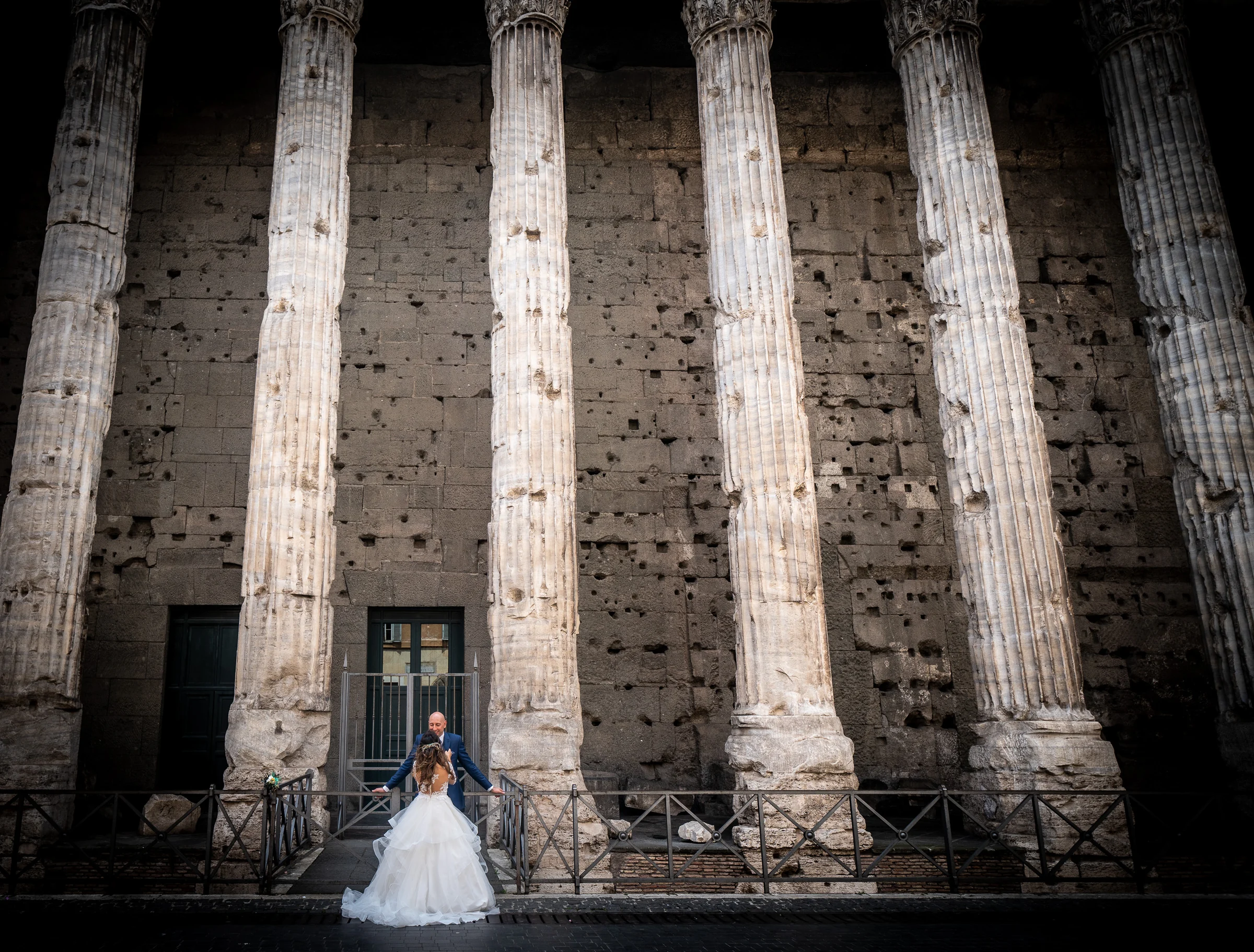 Marco y Esther posan a pequeña escala ante grandes columnas de la arquitectura histórica de Roma en una composición monumental.