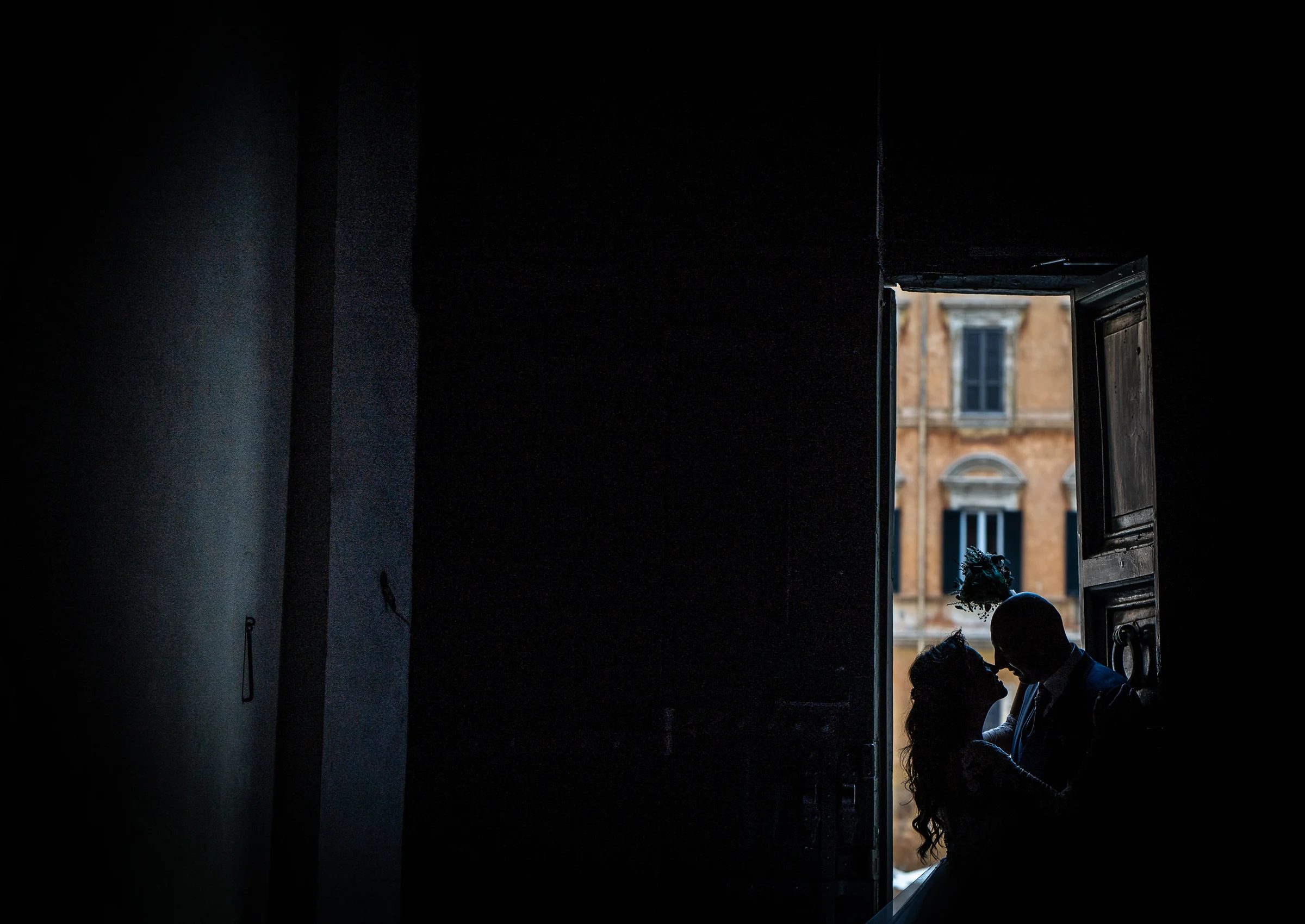 Silueta íntima de Marco y Esther recortada por la luz de una puerta durante su postboda en un edificio histórico de Roma.