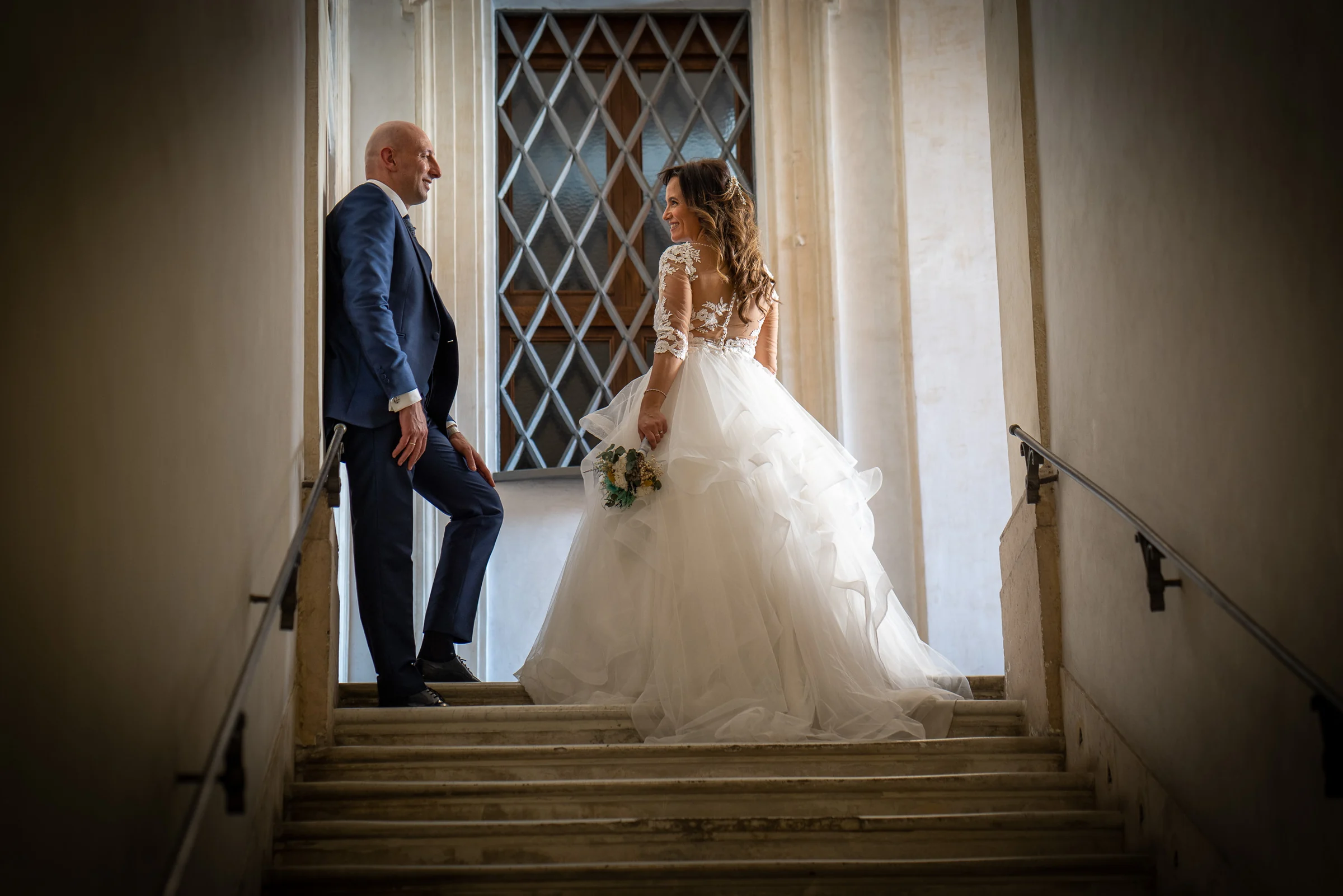 Marco y Esther se miran en una escalera interior de Roma, en un retrato elegante con arquitectura clásica y luz suave.