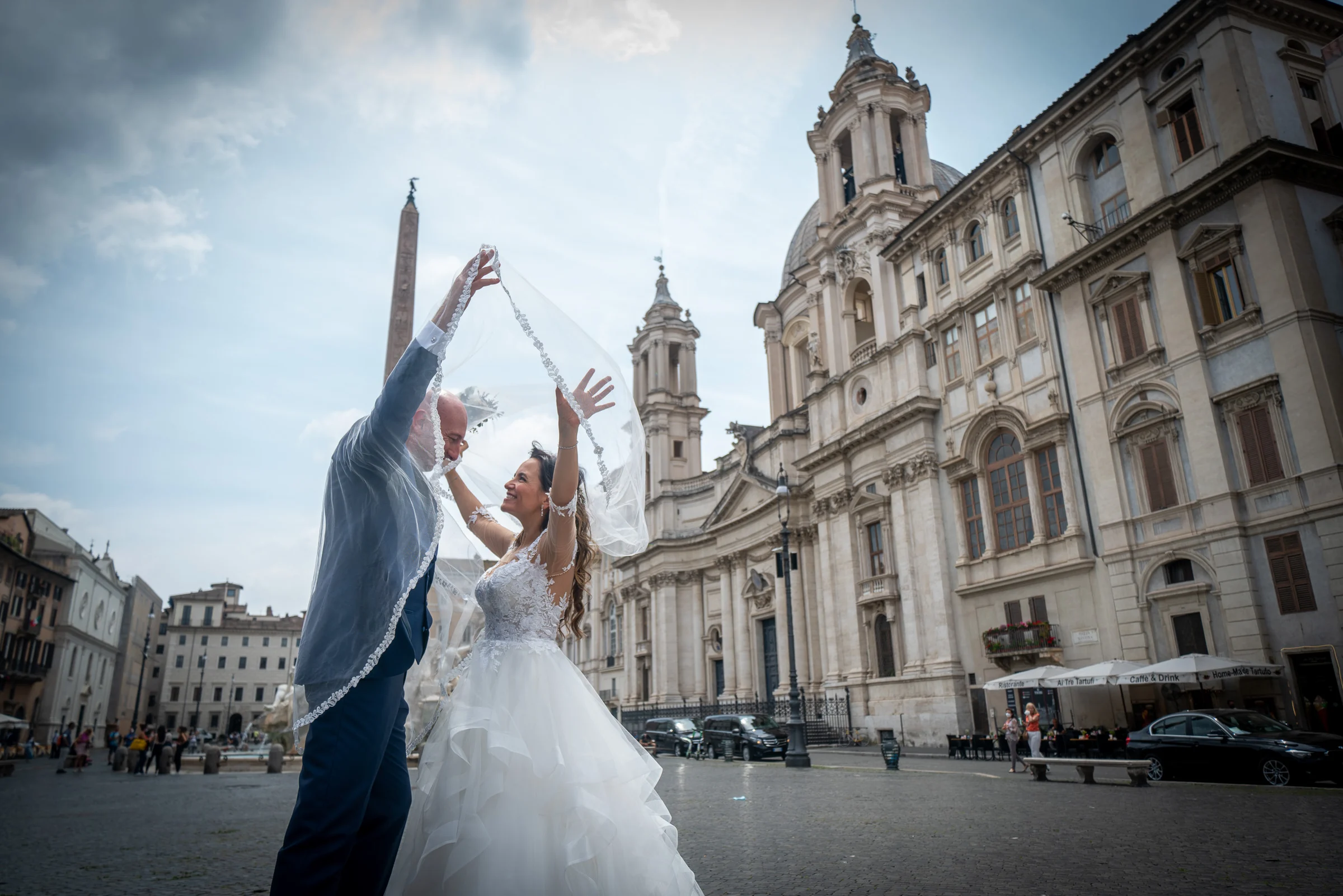 Marco y Esther juegan con el velo en Piazza Navona, rodeados por la arquitectura monumental del corazón histórico de Roma.