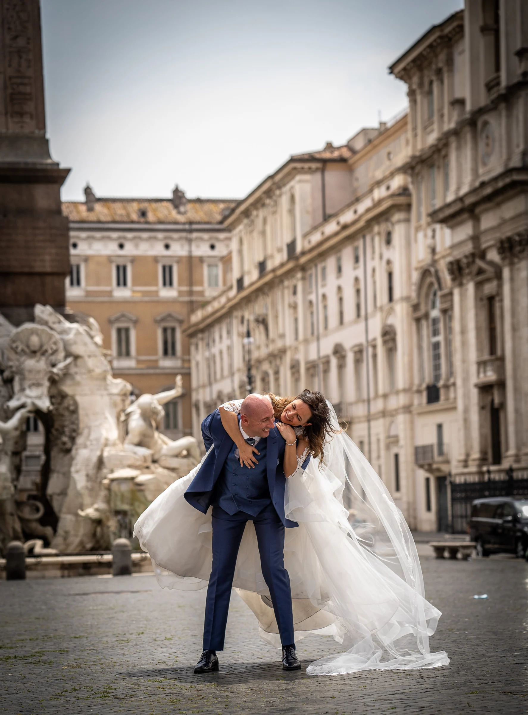 Marco y Esther ríen abrazados en Piazza Navona en una imagen natural y dinámica con la fuente histórica al fondo.