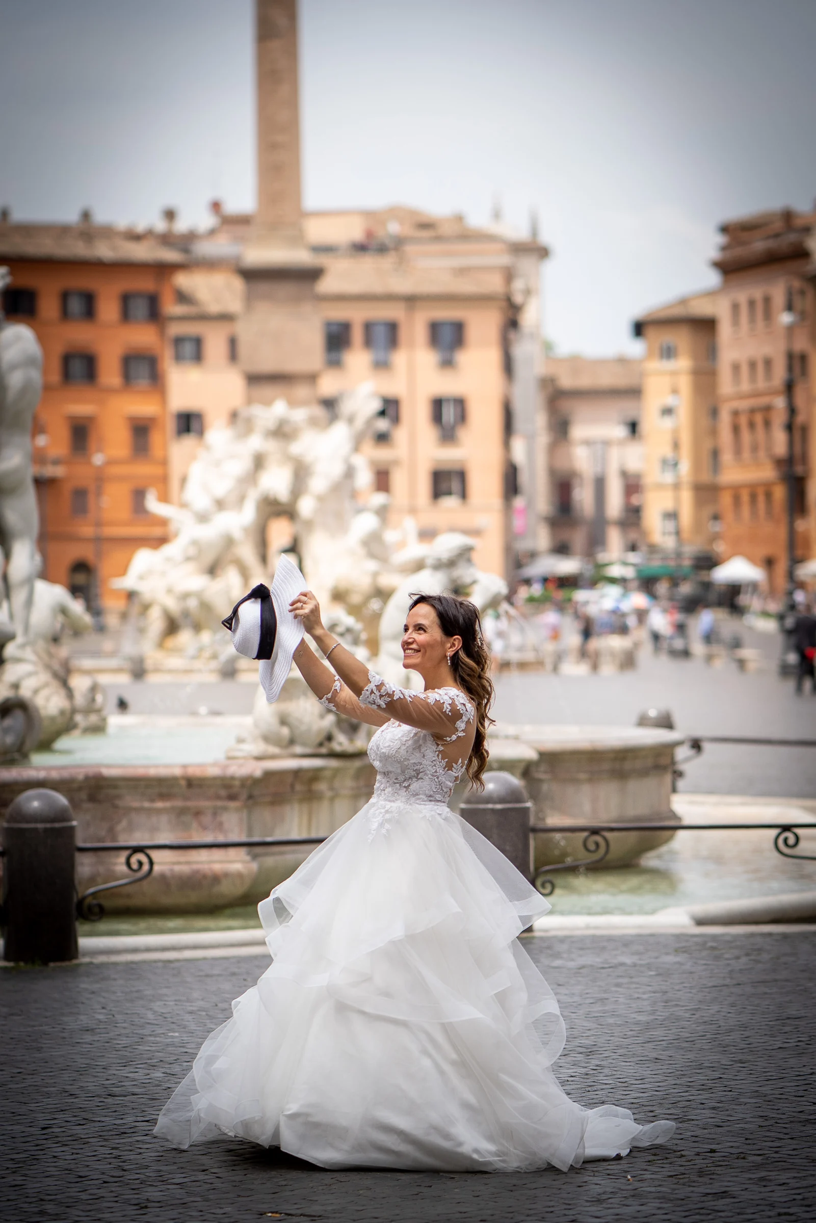 Esther levanta un sombrero junto a una de las fuentes de Piazza Navona en una escena alegre de su sesión postboda en Roma.