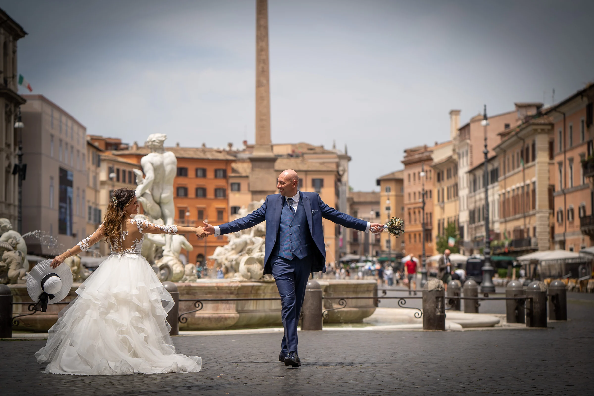 Marco y Esther caminan de la mano frente a las fuentes de Piazza Navona en un retrato amplio de su postboda romana.