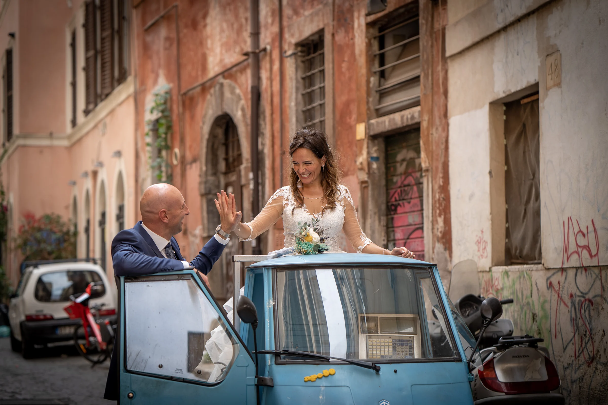 Marco y Esther se divierten junto a un clásico vehículo de tres ruedas azul durante su recorrido postboda por Roma.