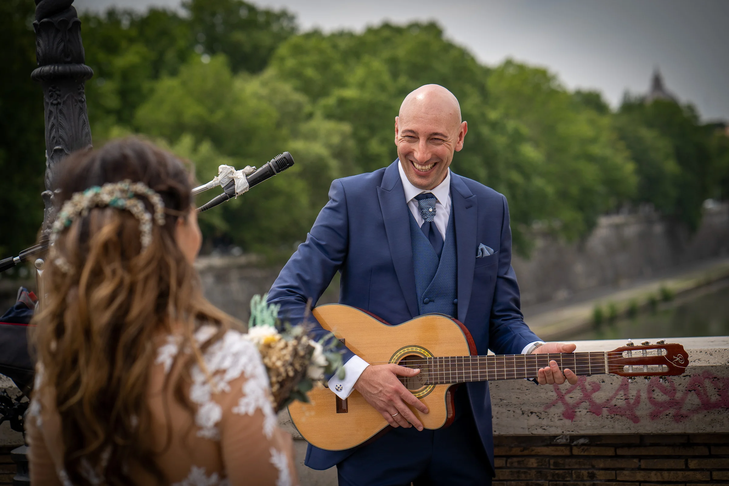 Marco sonríe con una guitarra junto a un músico callejero en un puente sobre el Tíber durante la sesión postboda.