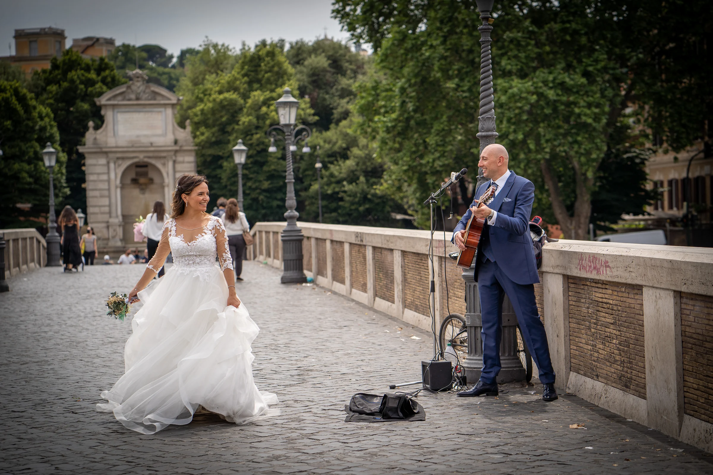 Esther escucha a un músico callejero mientras Marco toca la guitarra en un puente romano, un momento espontáneo del reportaje.