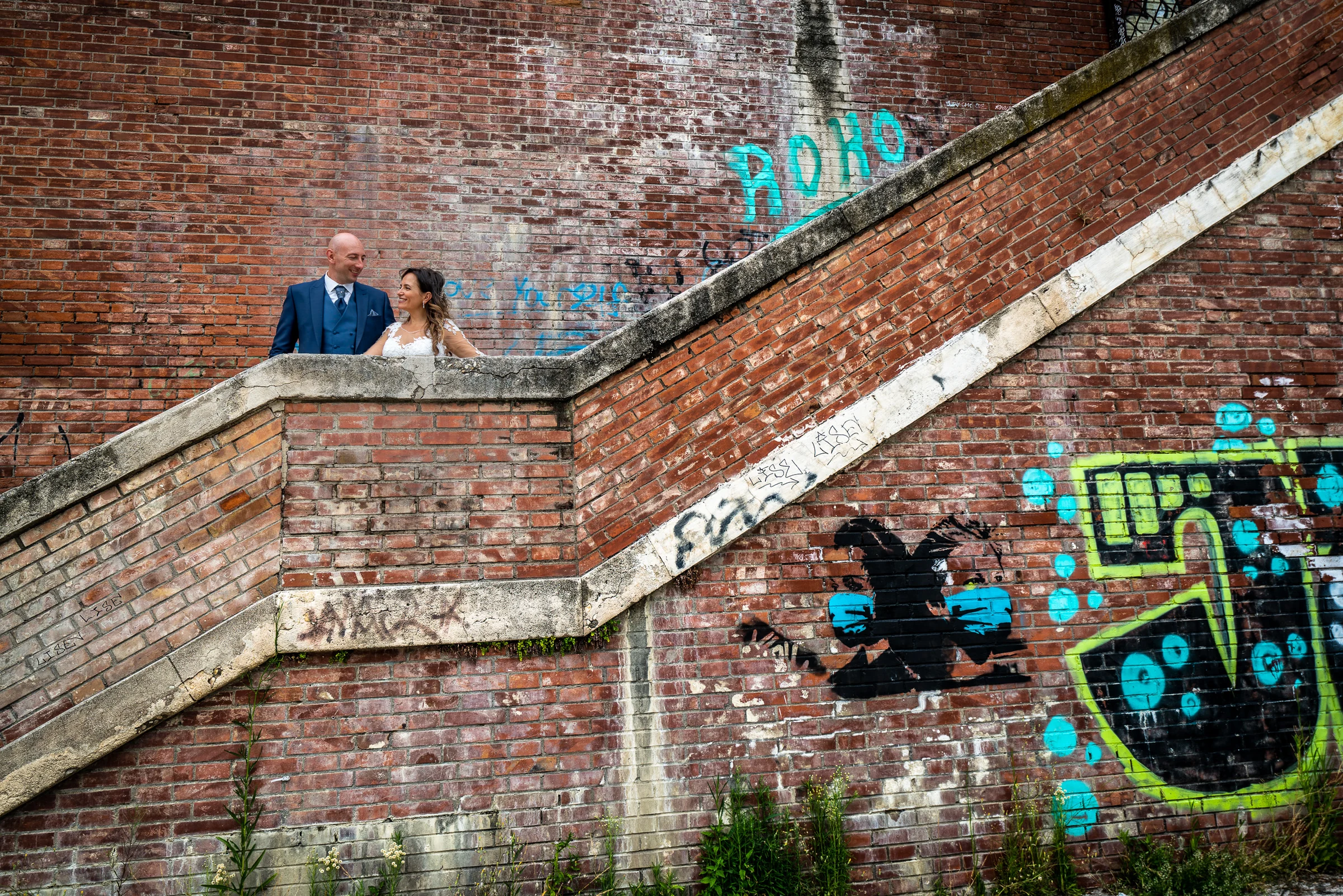 Marco y Esther aparecen entre escaleras de ladrillo y grafitis junto al Tíber en una composición urbana y geométrica.