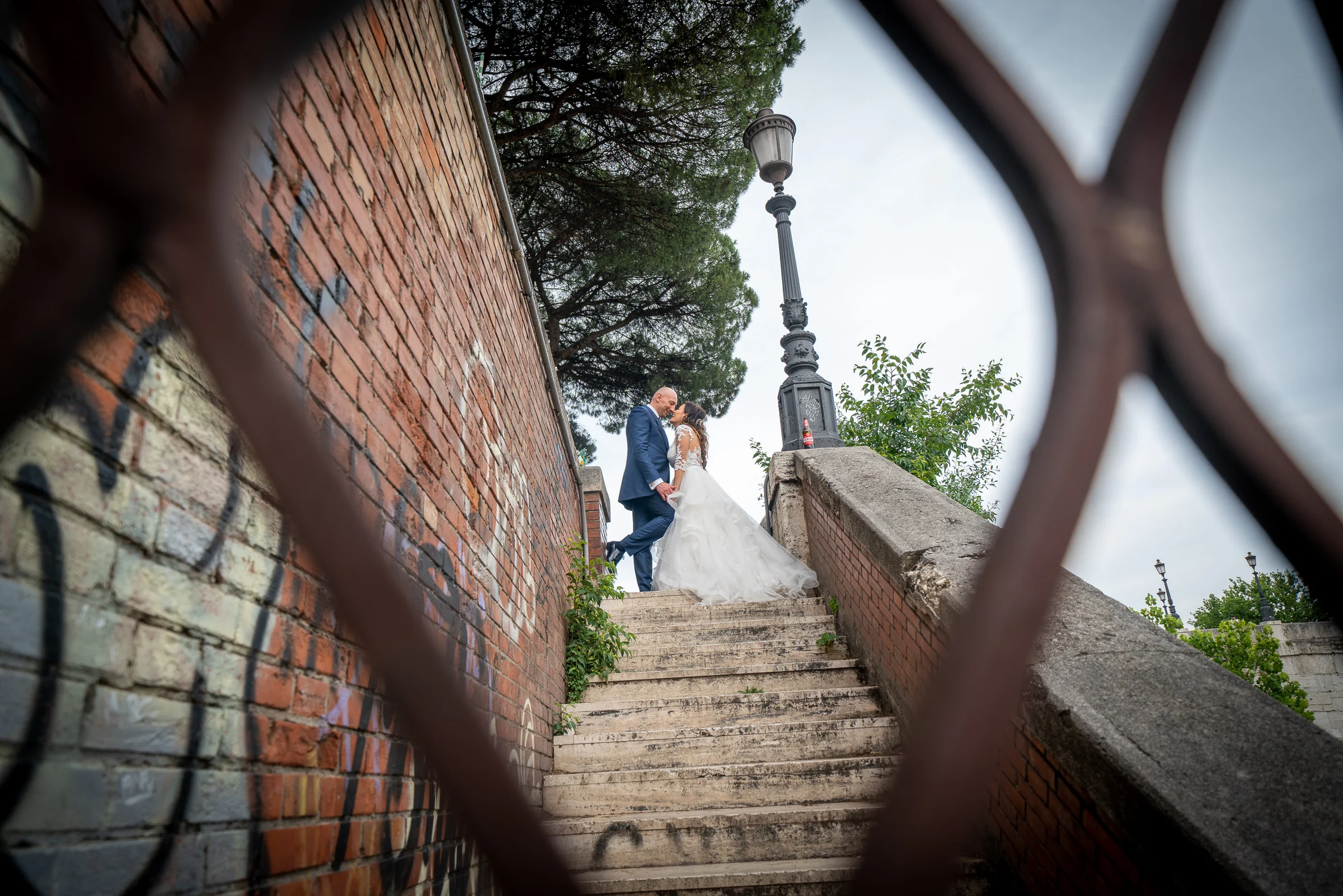 Marco y Esther se besan en una escalera junto al Tíber vistos a través de una estructura metálica desenfocada.