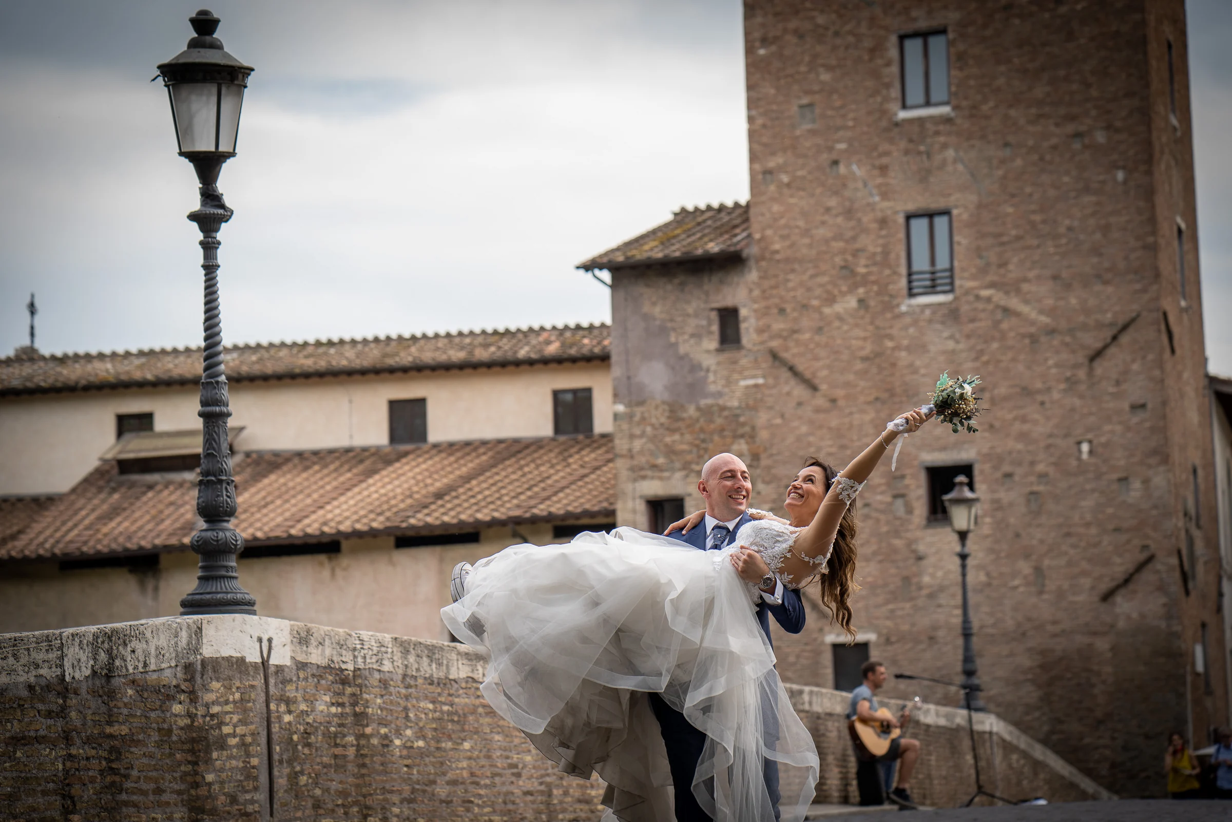 Marco lleva a Esther en brazos sobre un puente de piedra de Roma en una fotografía alegre y elegante.