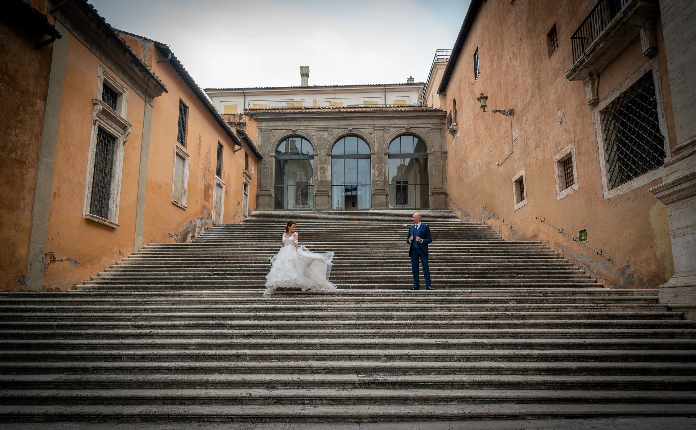 Marco y Esther aparecen separados en una gran escalinata romana, integrados en la simetría del entorno.