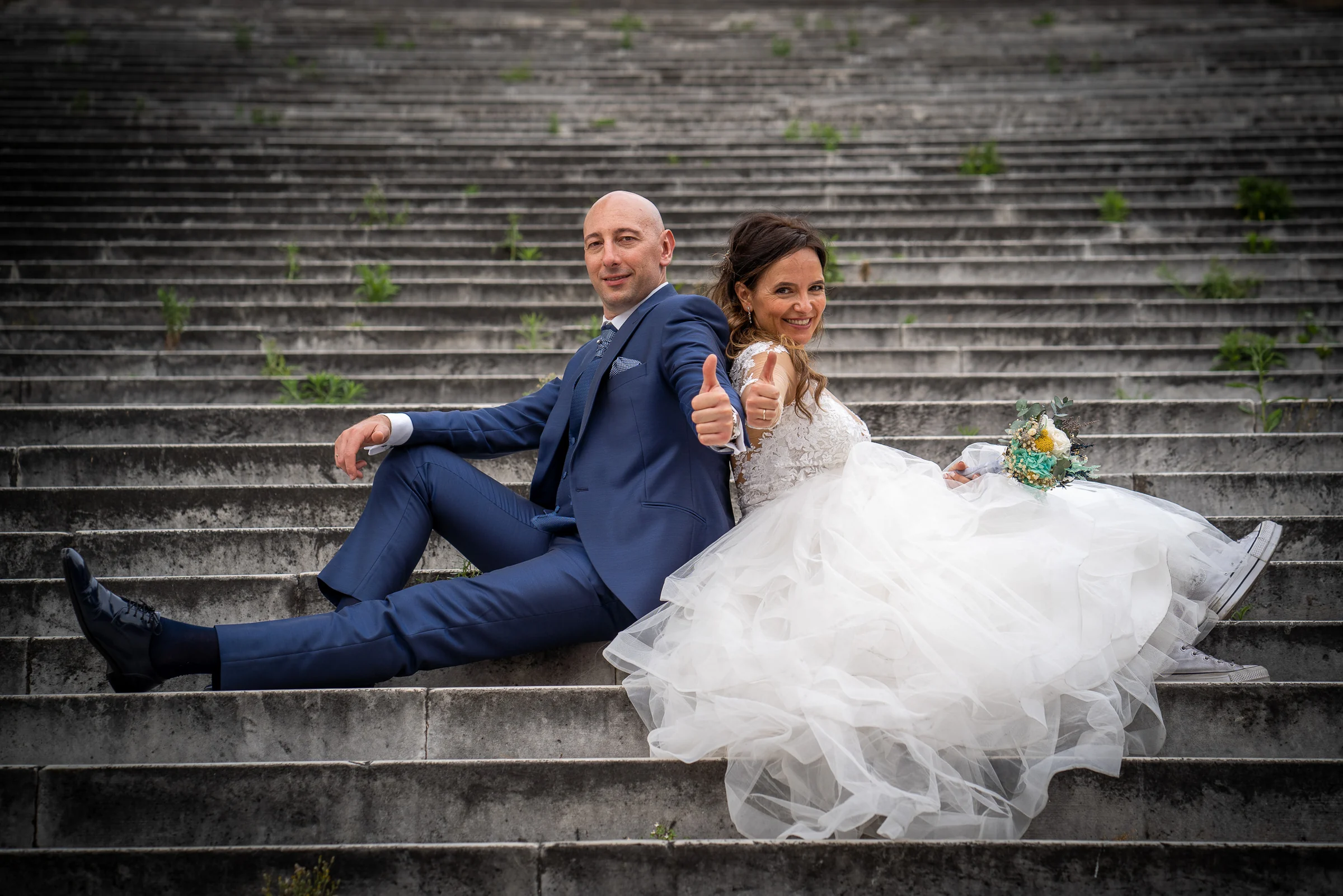 Marco y Esther se sientan espalda con espalda en una gran escalinata de piedra y sonríen a cámara.