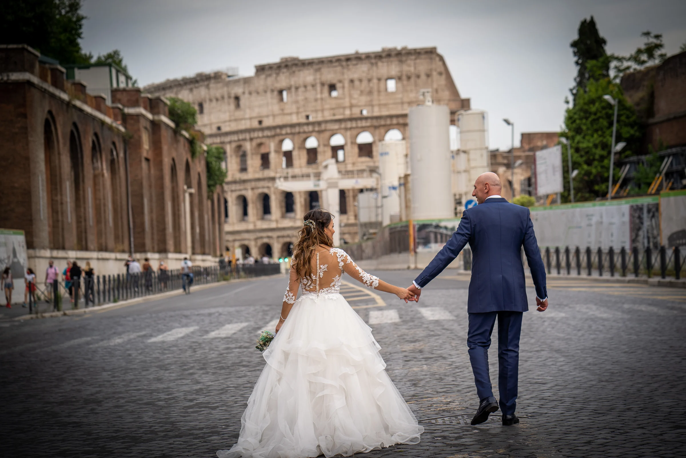 Marco y Esther caminan de la mano hacia el Coliseo de Roma en una imagen amplia de su postboda.