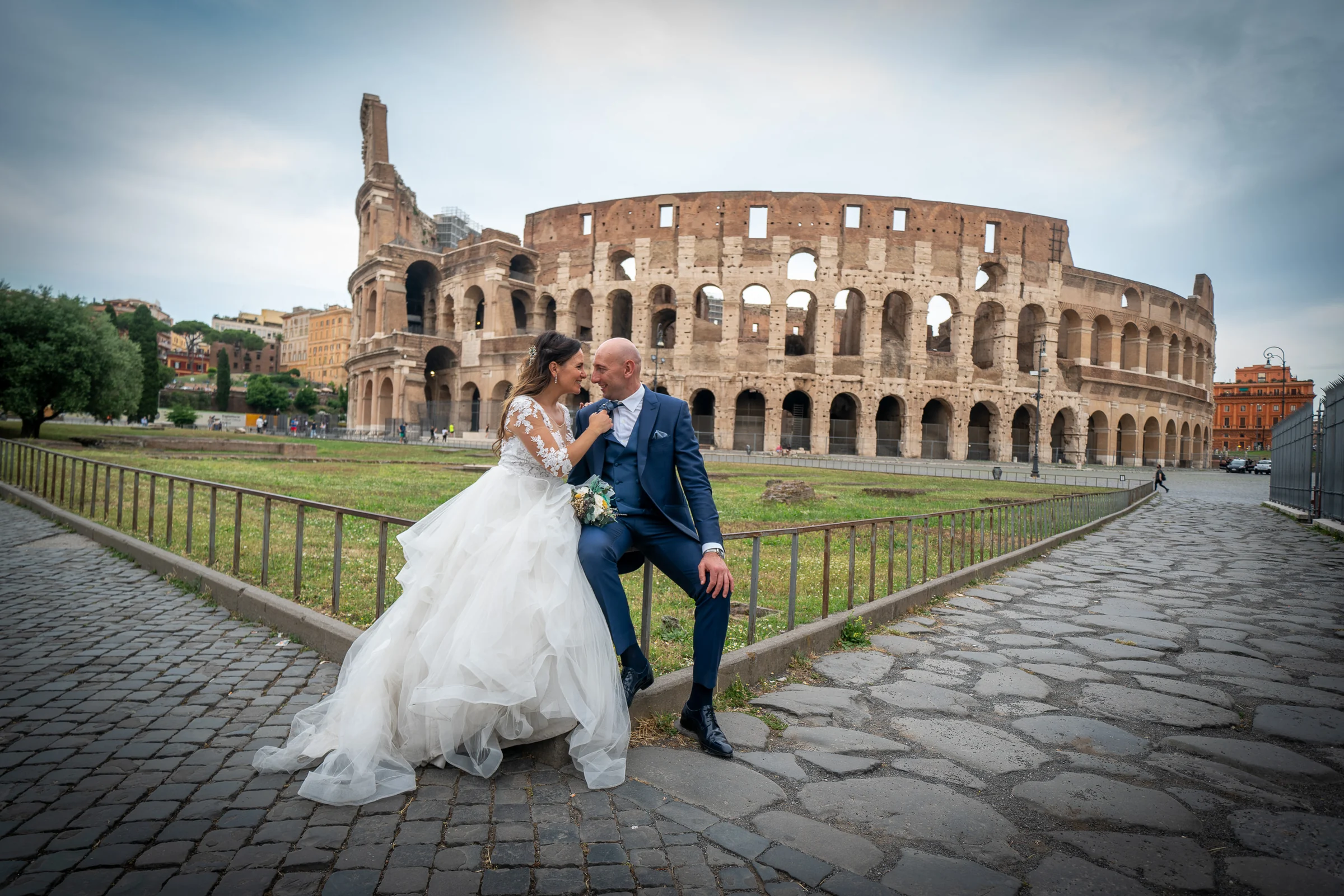 Marco y Esther posan juntos con el Coliseo al fondo sobre el pavimento histórico de Roma.