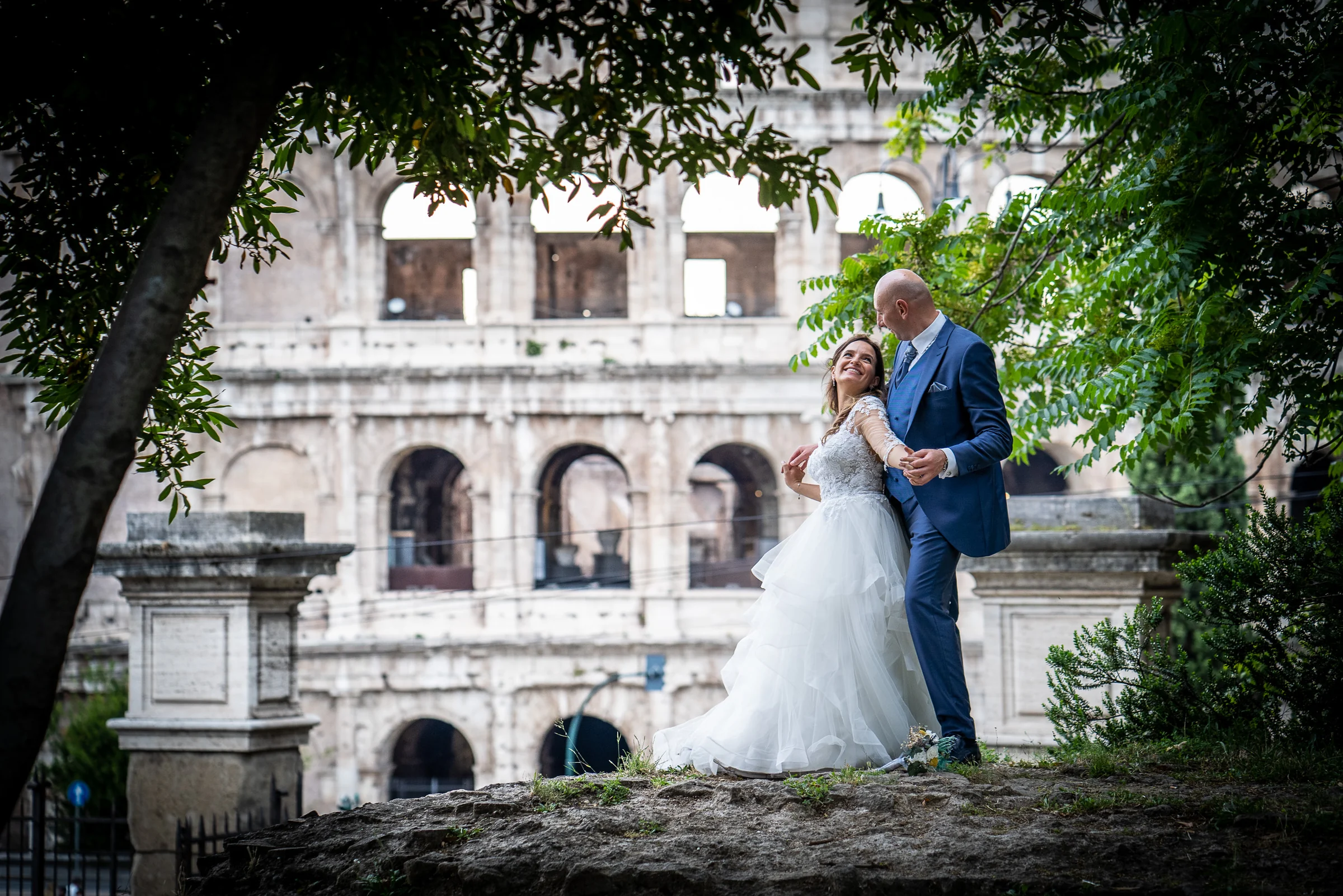 Marco y Esther se miran entre árboles con el Coliseo de Roma enmarcado al fondo durante su sesión postboda.
