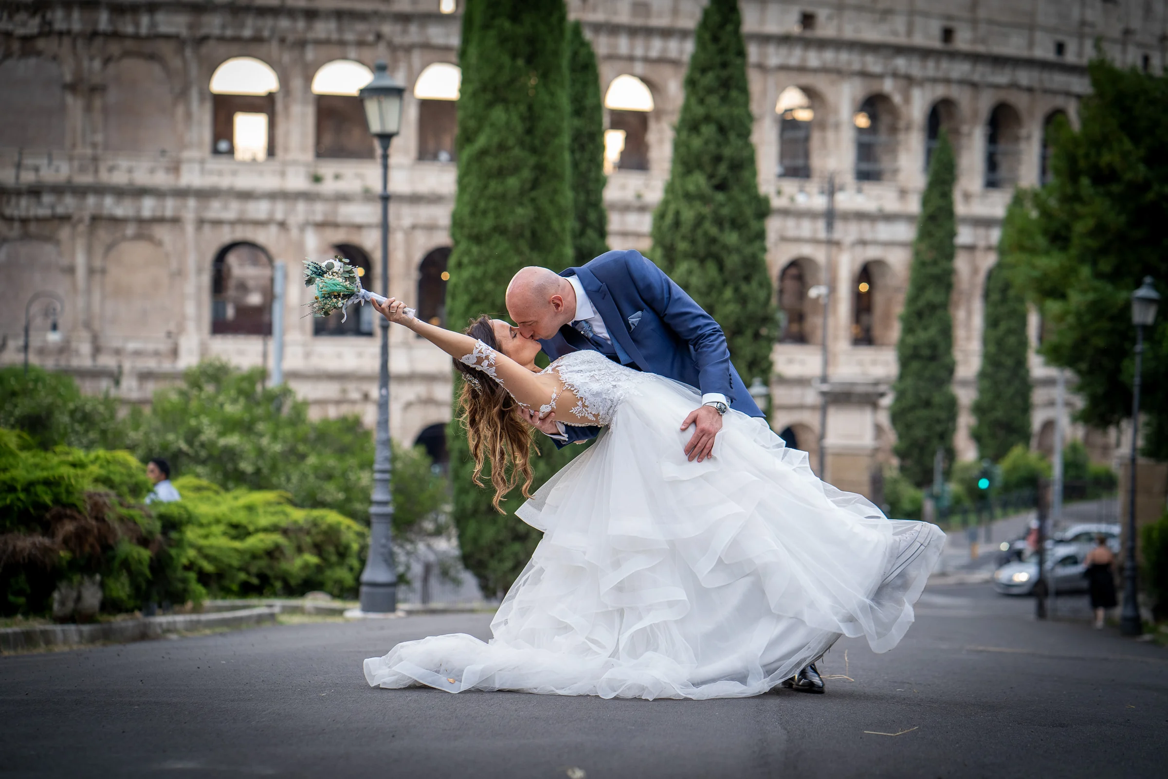 Marco inclina a Esther en un beso frente al Coliseo de Roma en una fotografía romántica y dinámica.