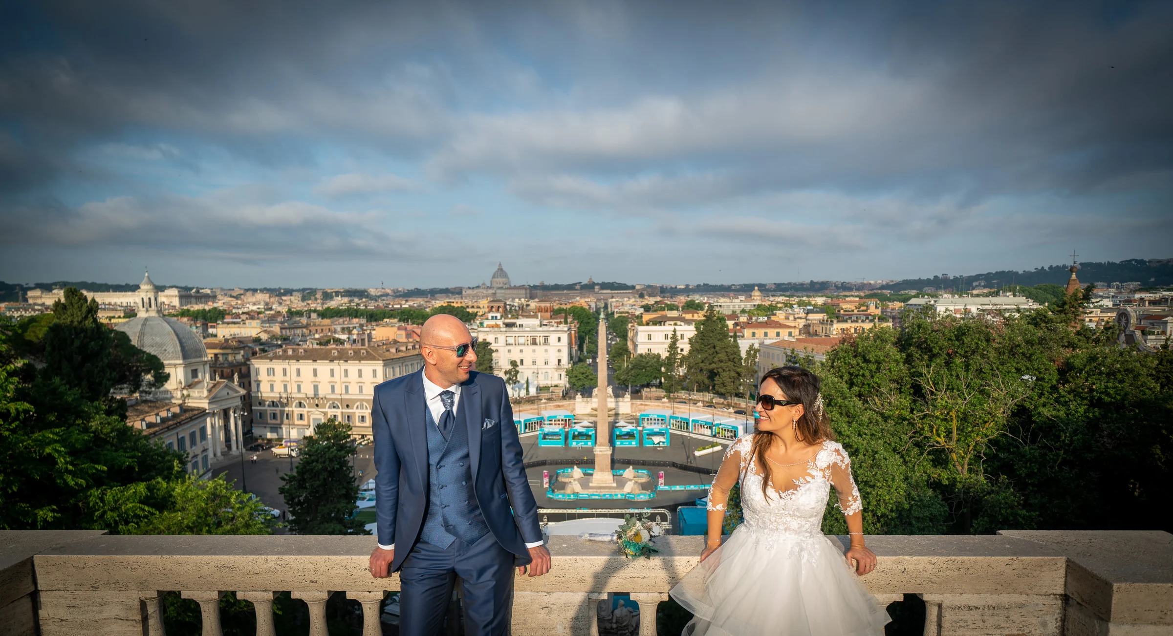 Marco y Esther descansan en un mirador panorámico con los tejados y monumentos de Roma extendiéndose al fondo.