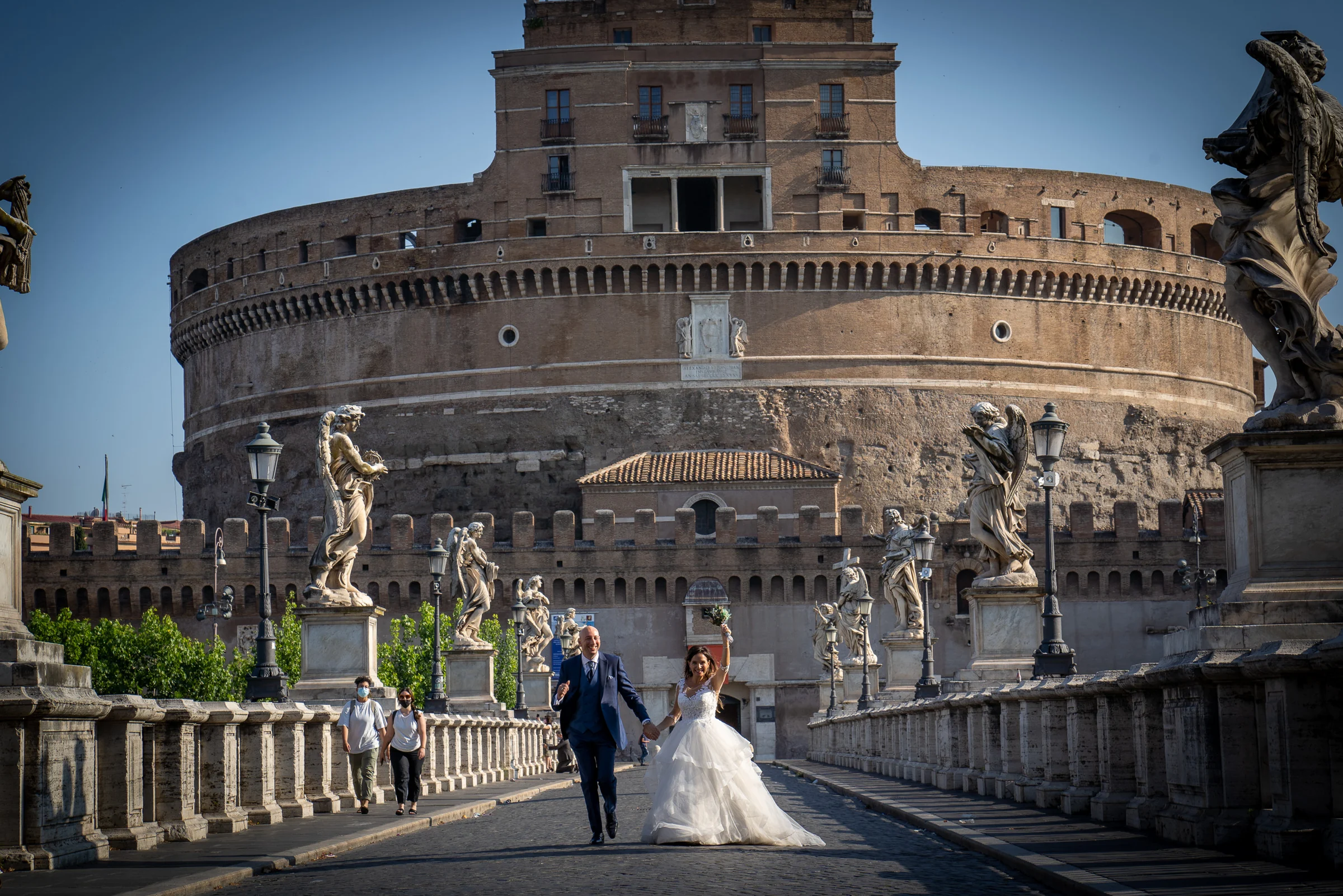 Marco y Esther caminan por el puente frente a Castel Sant'Angelo, rodeados por sus esculturas históricas.