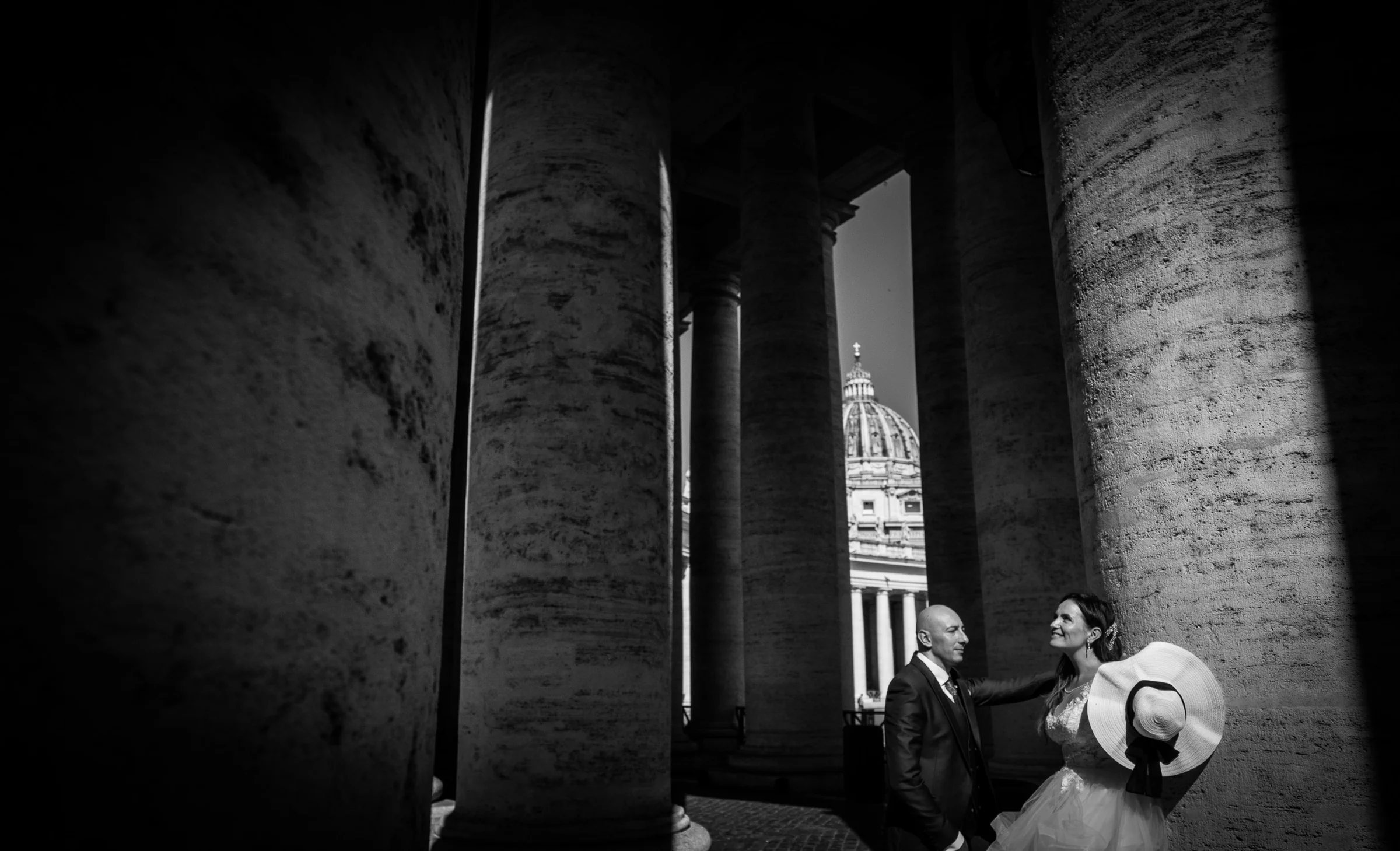 Retrato en blanco y negro de Marco y Esther entre las columnas de la Plaza de San Pedro con la cúpula al fondo.