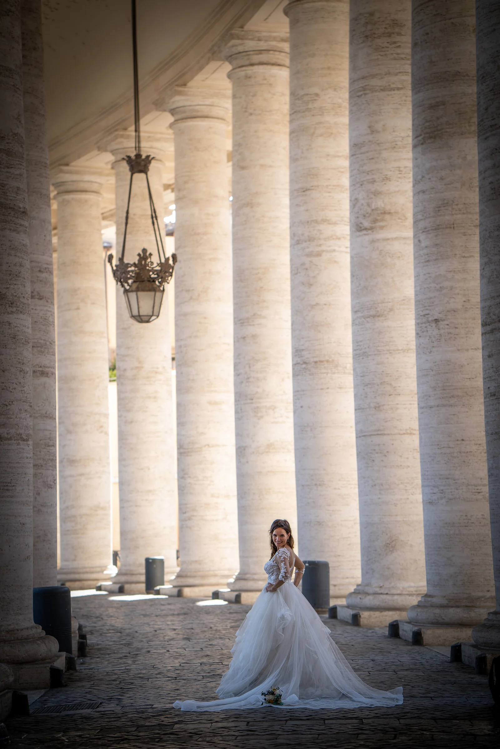 Esther posa sola entre las monumentales columnas de la Plaza de San Pedro en un retrato vertical de novia.