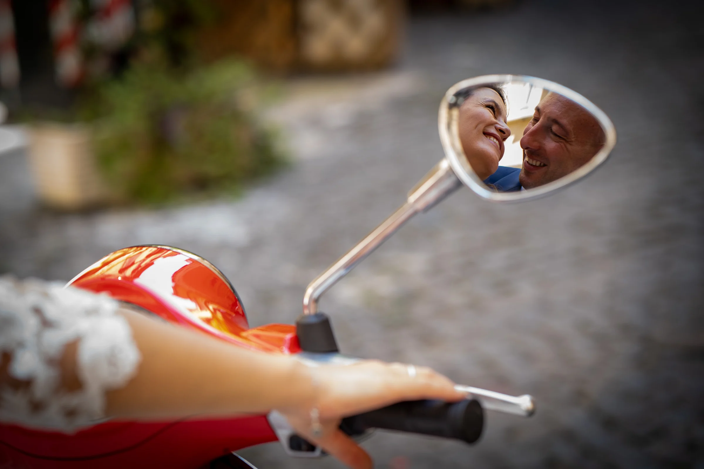 El rostro sonriente de Marco se refleja en el espejo de una Vespa roja junto a Esther durante la postboda.