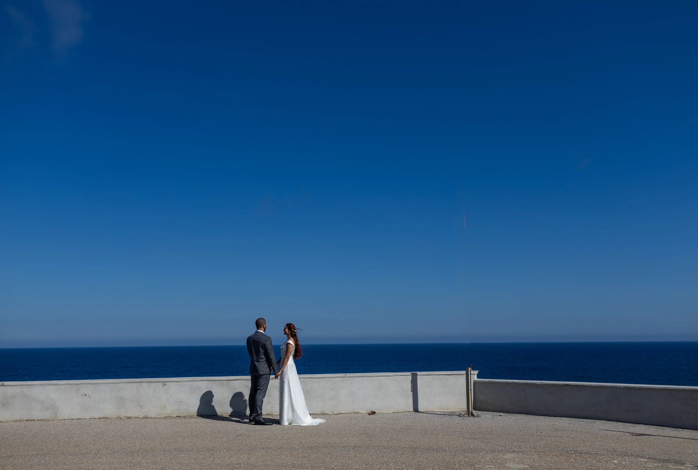 Noemí y Fran se dan la mano en un amplio mirador con el mar al fondo durante su postboda en Cartagena.