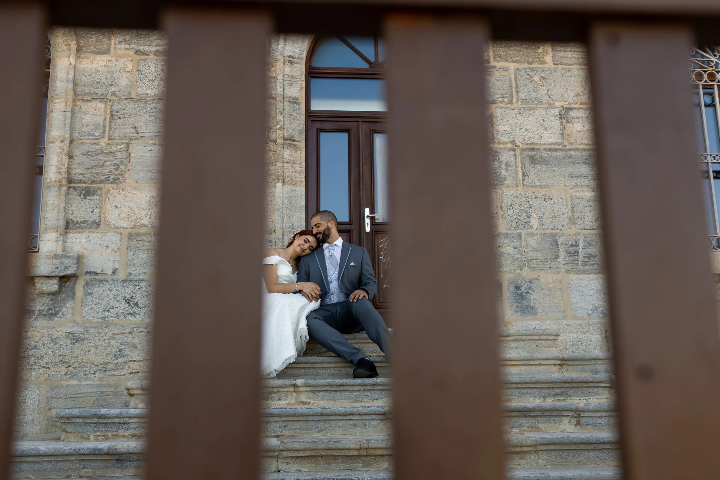 Noemí y Fran descansan abrazados en una escalinata de piedra, fotografiados entre barrotes, en Cartagena.