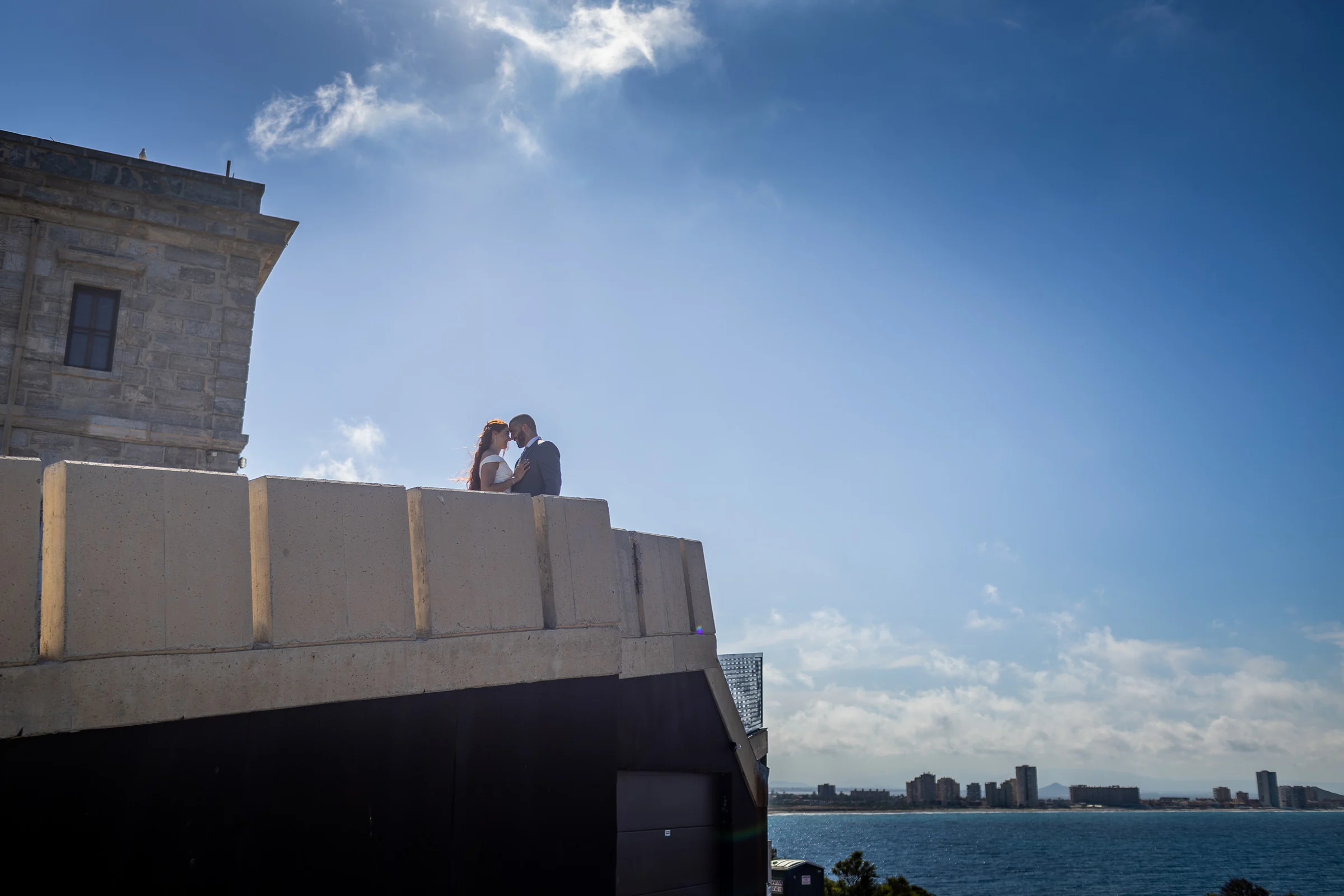 Noemí y Fran se abrazan sobre una fortaleza con vistas al mar y al skyline de Cartagena.