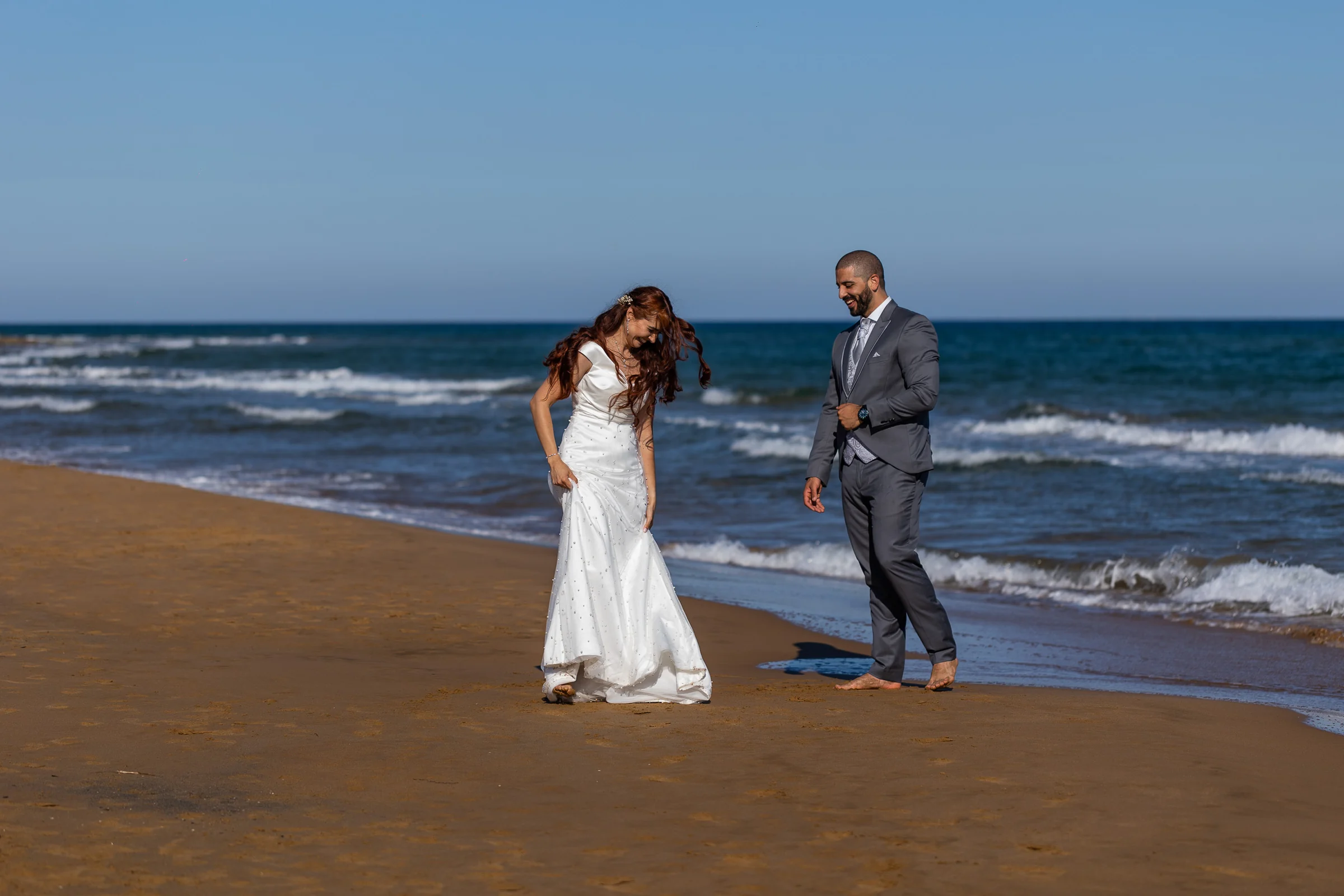 Noemí y Fran sonríen mientras caminan por la arena junto al mar durante su postboda en Cartagena.