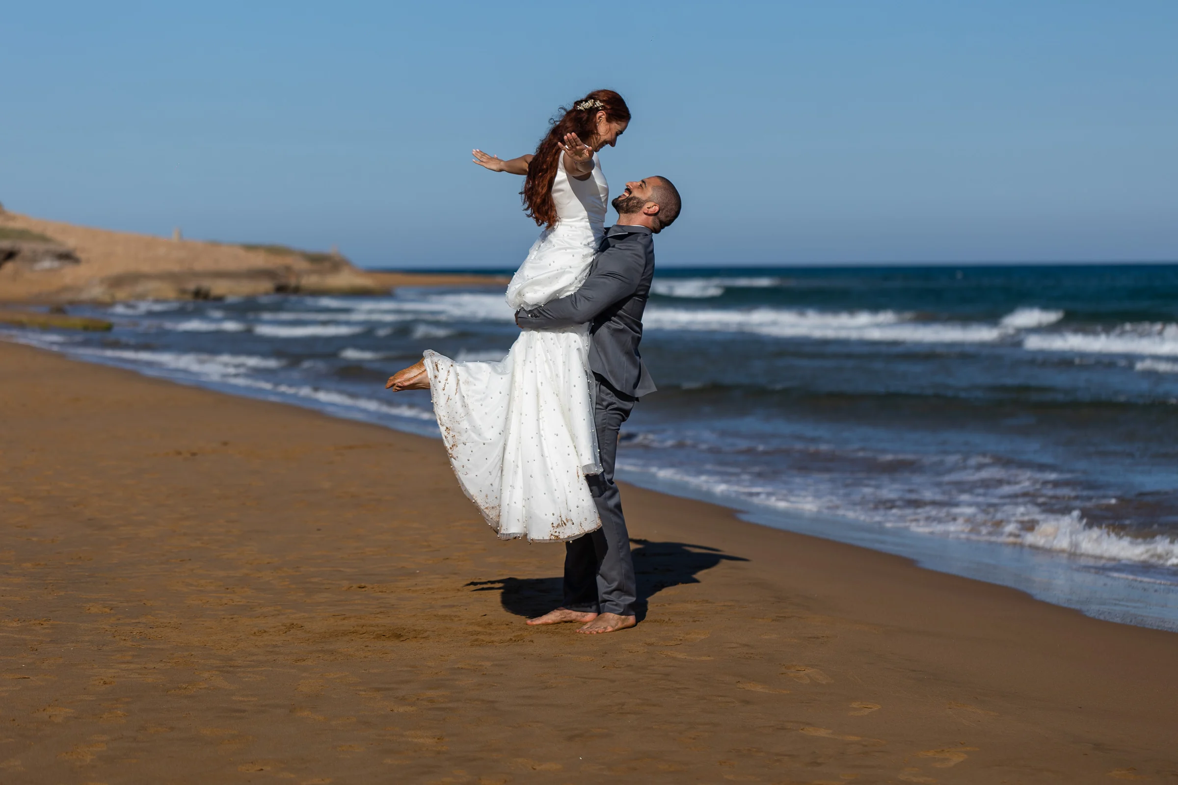 Fran levanta a Noemí en brazos sobre la arena durante su postboda en la playa de Cartagena.